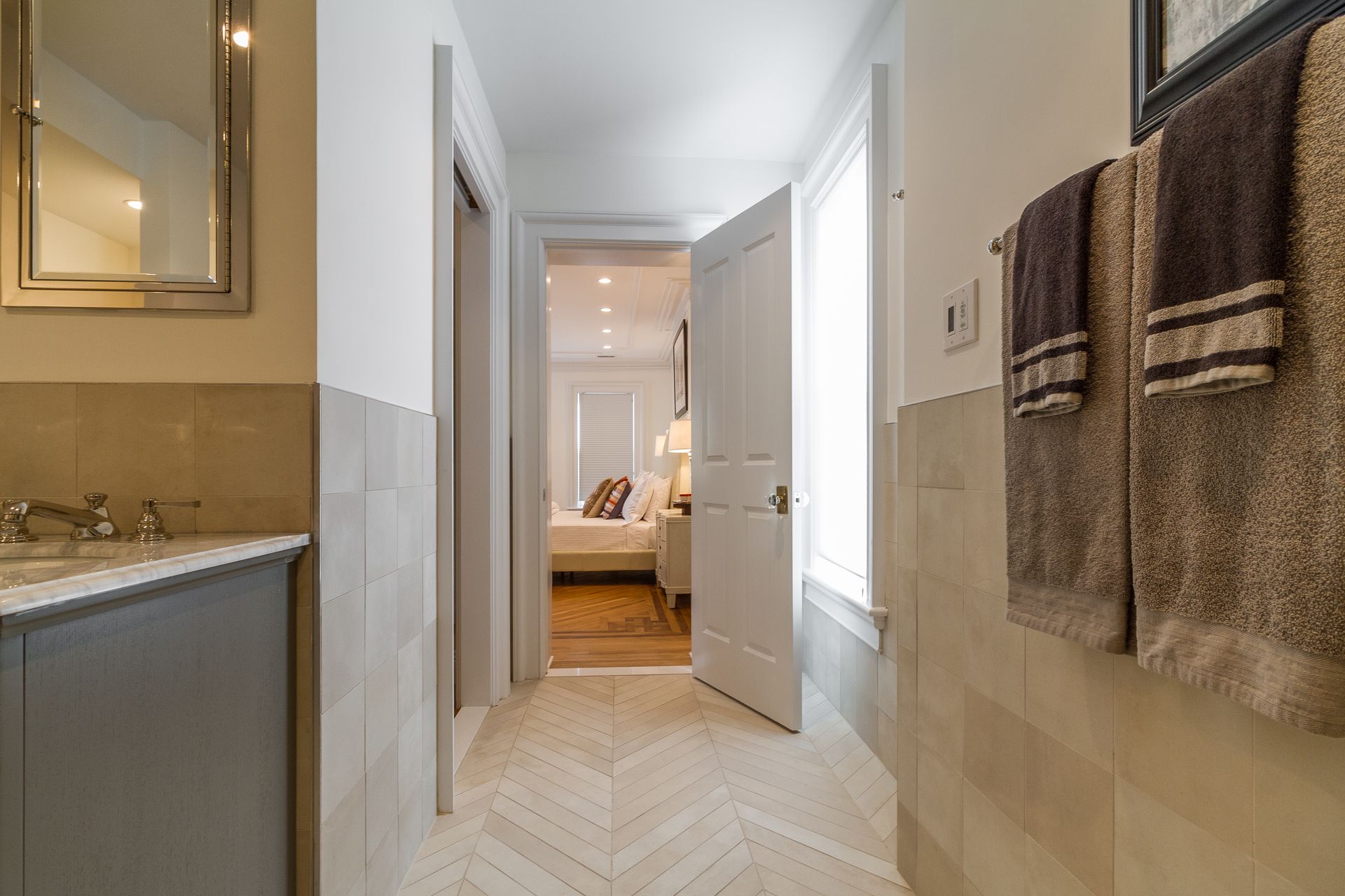 Bathroom hallway with open doorway to bedroom; towels on the right, vanity on the left.
