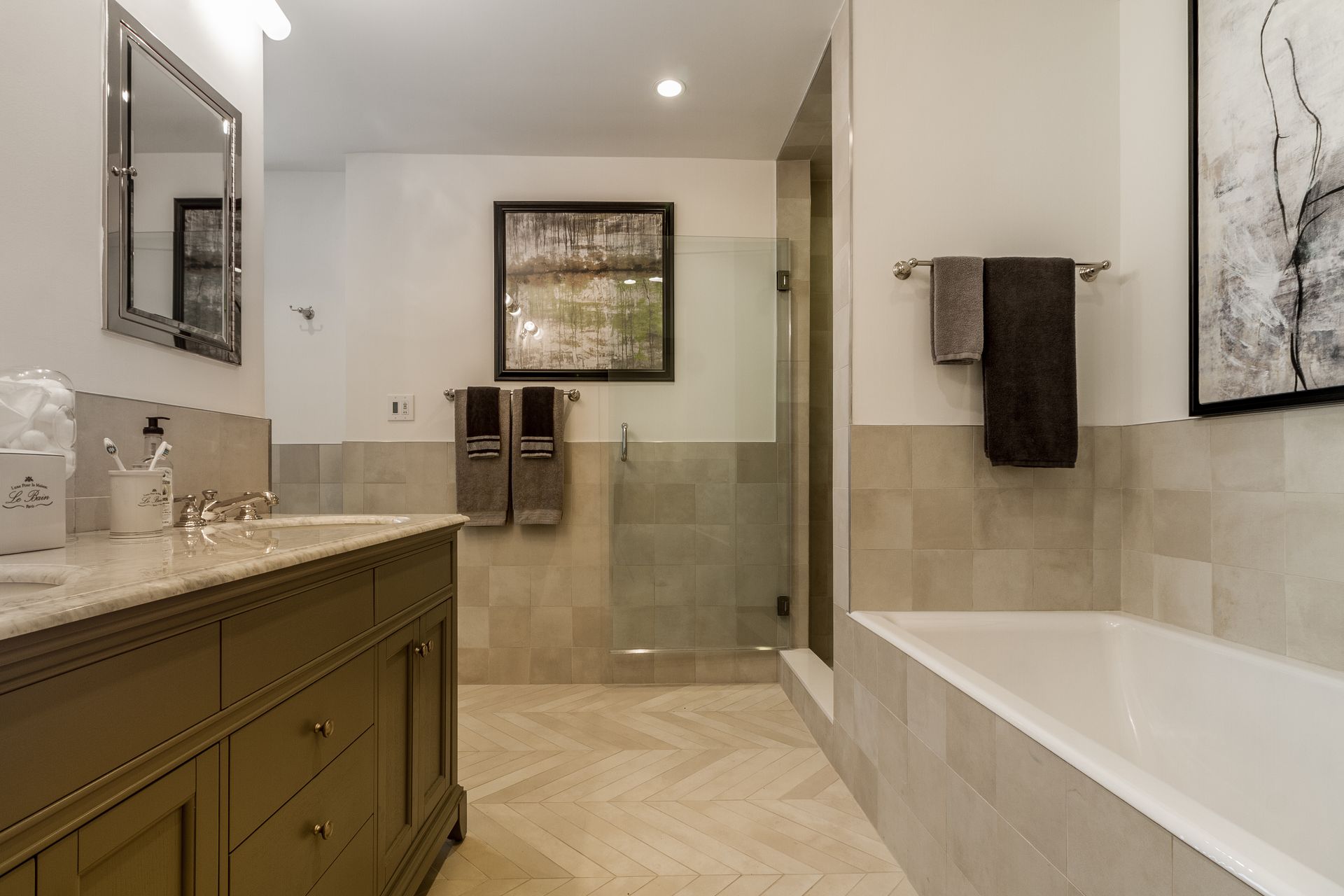 A modern bathroom with a double vanity, shower, and a soaking tub. Neutral tones, herringbone floor.