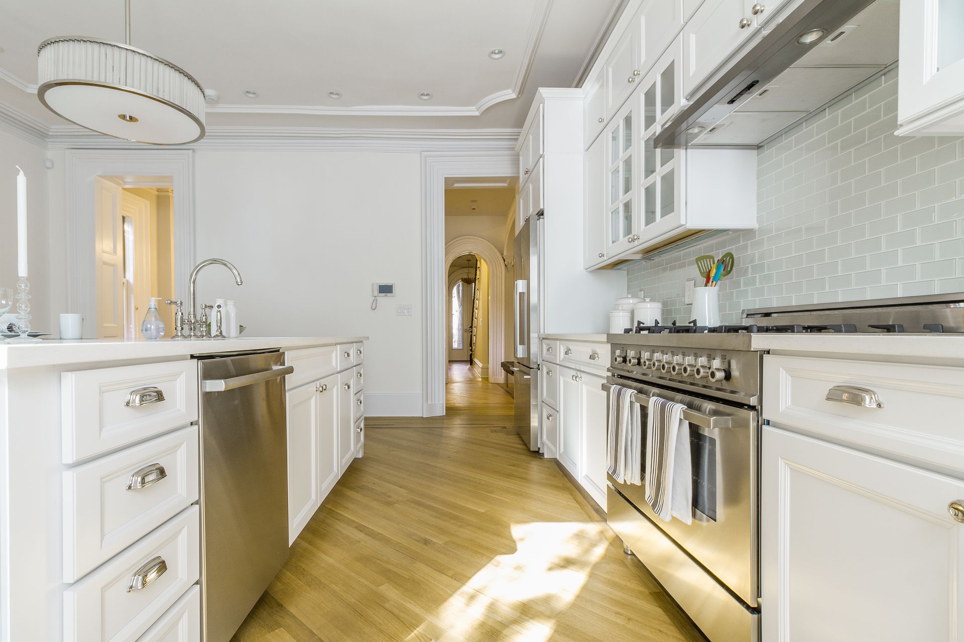 Bright white kitchen with stainless steel appliances, light wood floors, and blue tile backsplash.