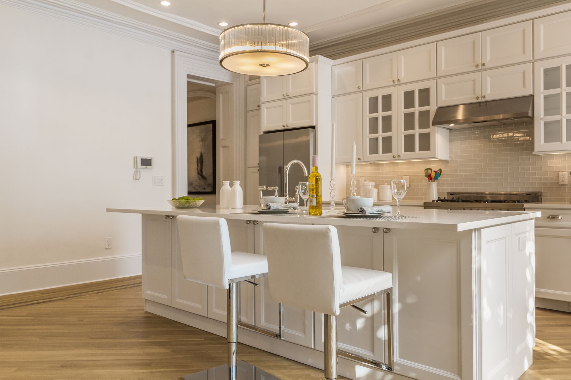 White kitchen with island and two bar stools, light fixture overhead.