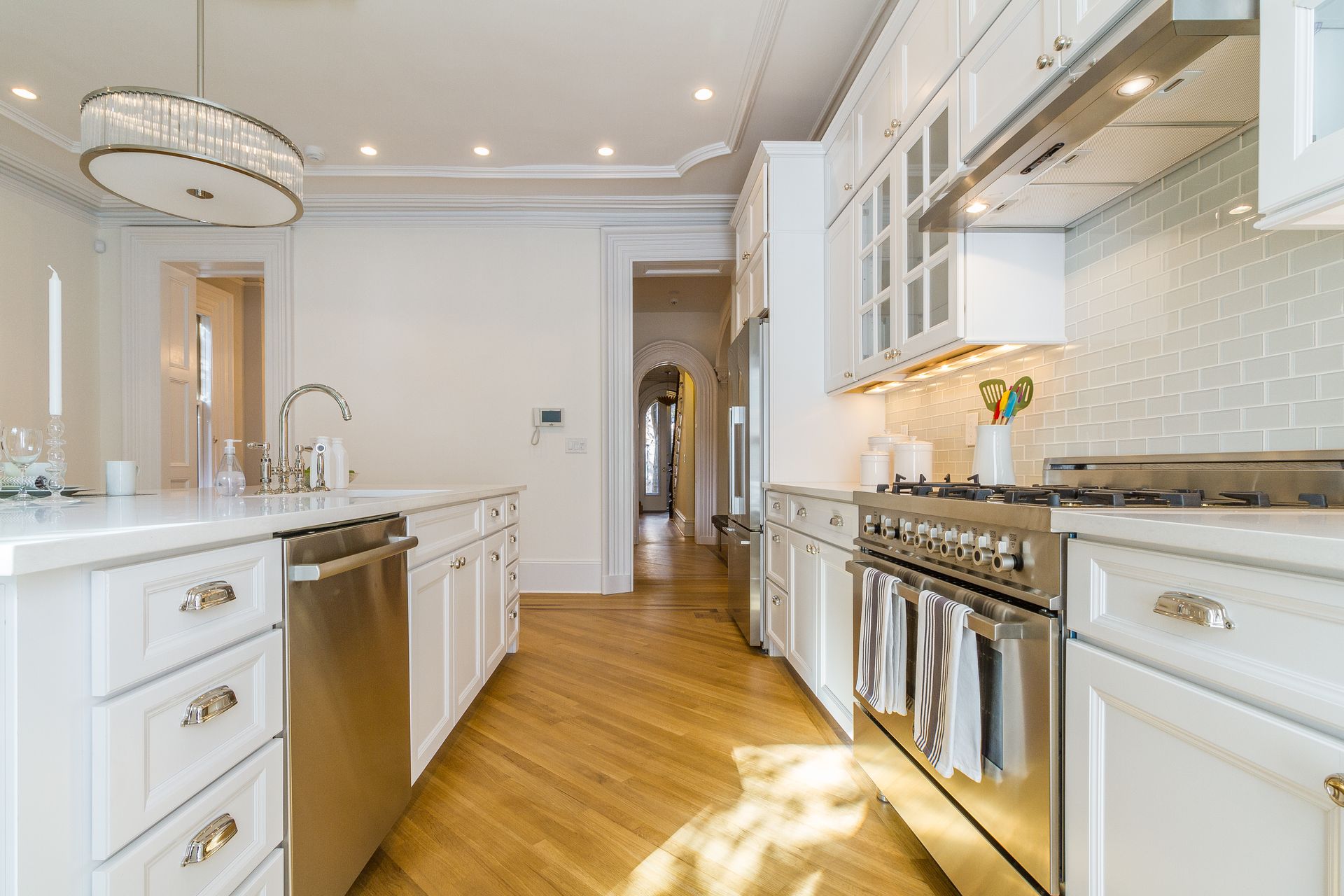 Bright white kitchen with stainless steel appliances, a center island, and hardwood floors.