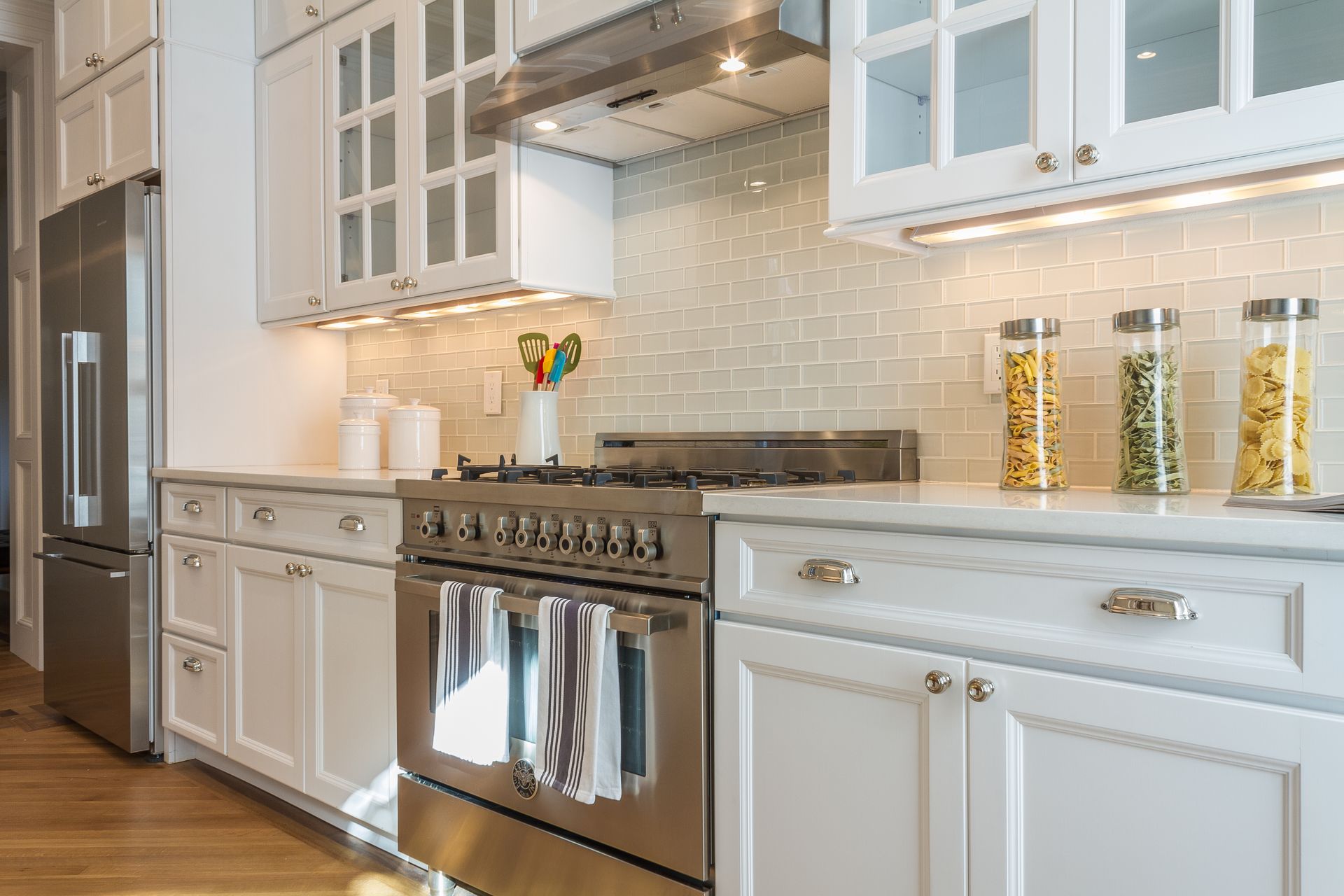 White kitchen with stainless steel appliances, marble countertops, and glass-front cabinets.