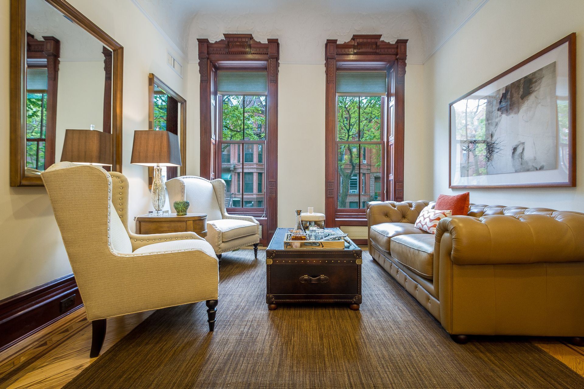 Living room with leather sofa, two armchairs, a trunk coffee table, and windows.