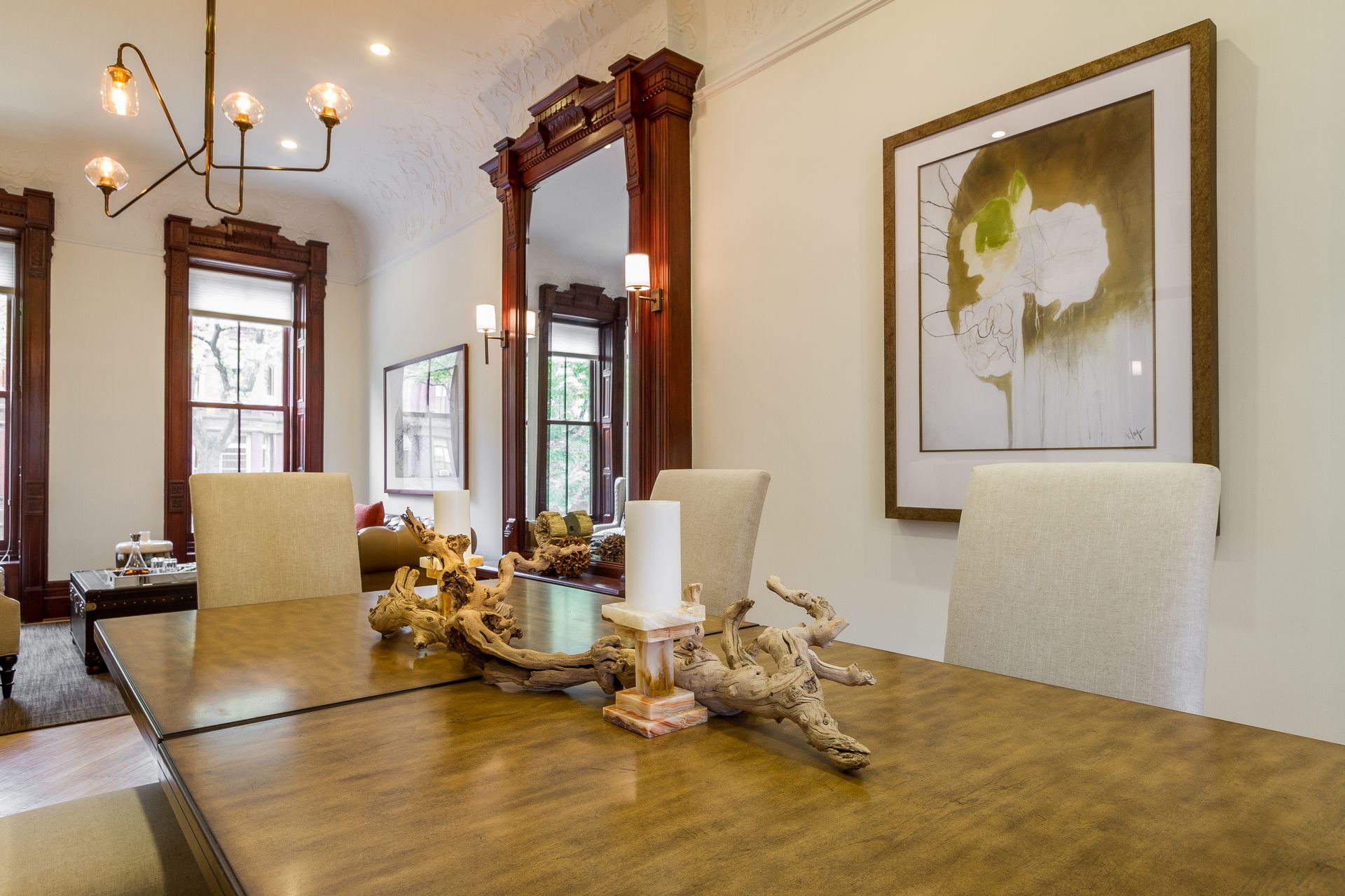 Dining room with wood table, chairs, large mirror, artwork, and modern chandelier.