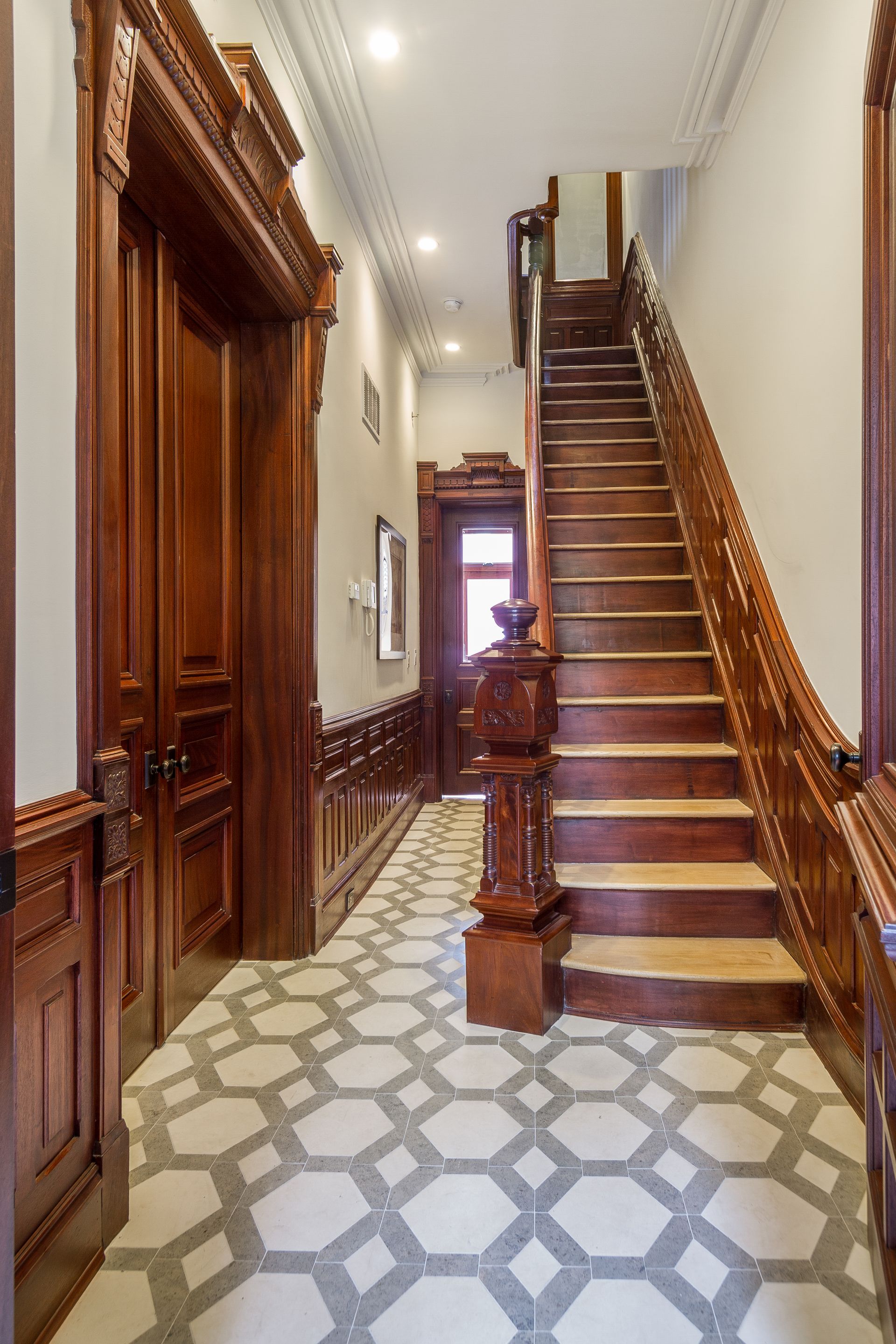 Elegant hallway with wooden staircase, ornate molding, and patterned tile floor.