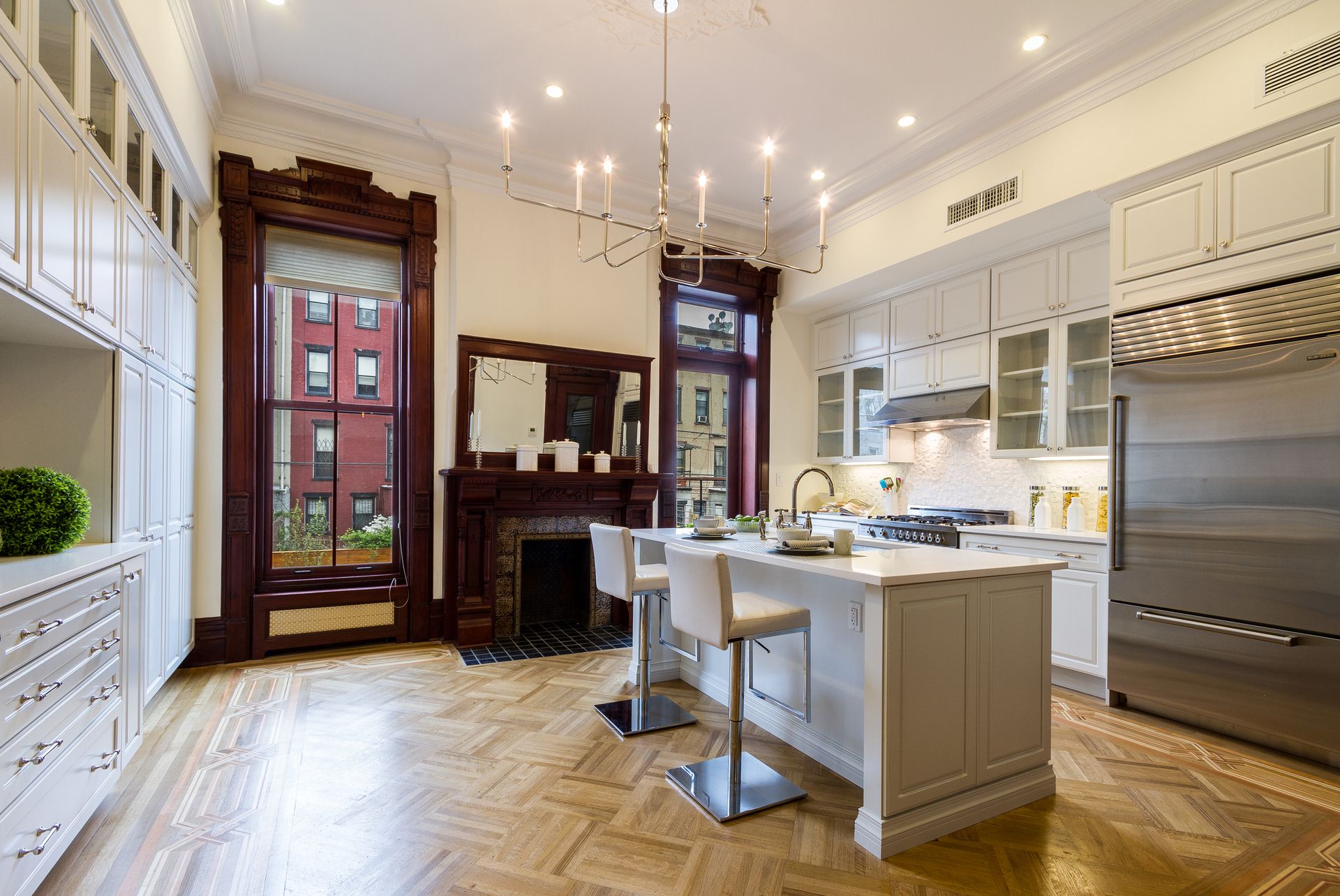 Elegant kitchen with white cabinets, island, wooden floor, and a fireplace.