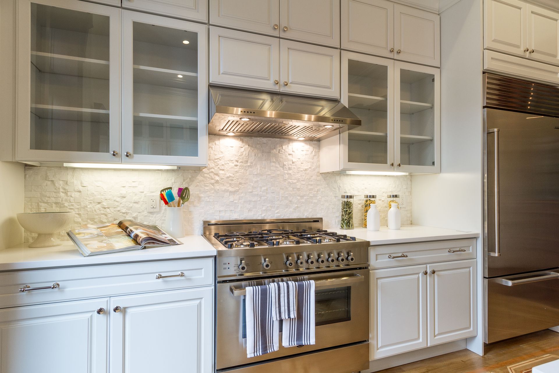 White kitchen with stainless steel appliances, upper glass-door cabinets, and white countertops.