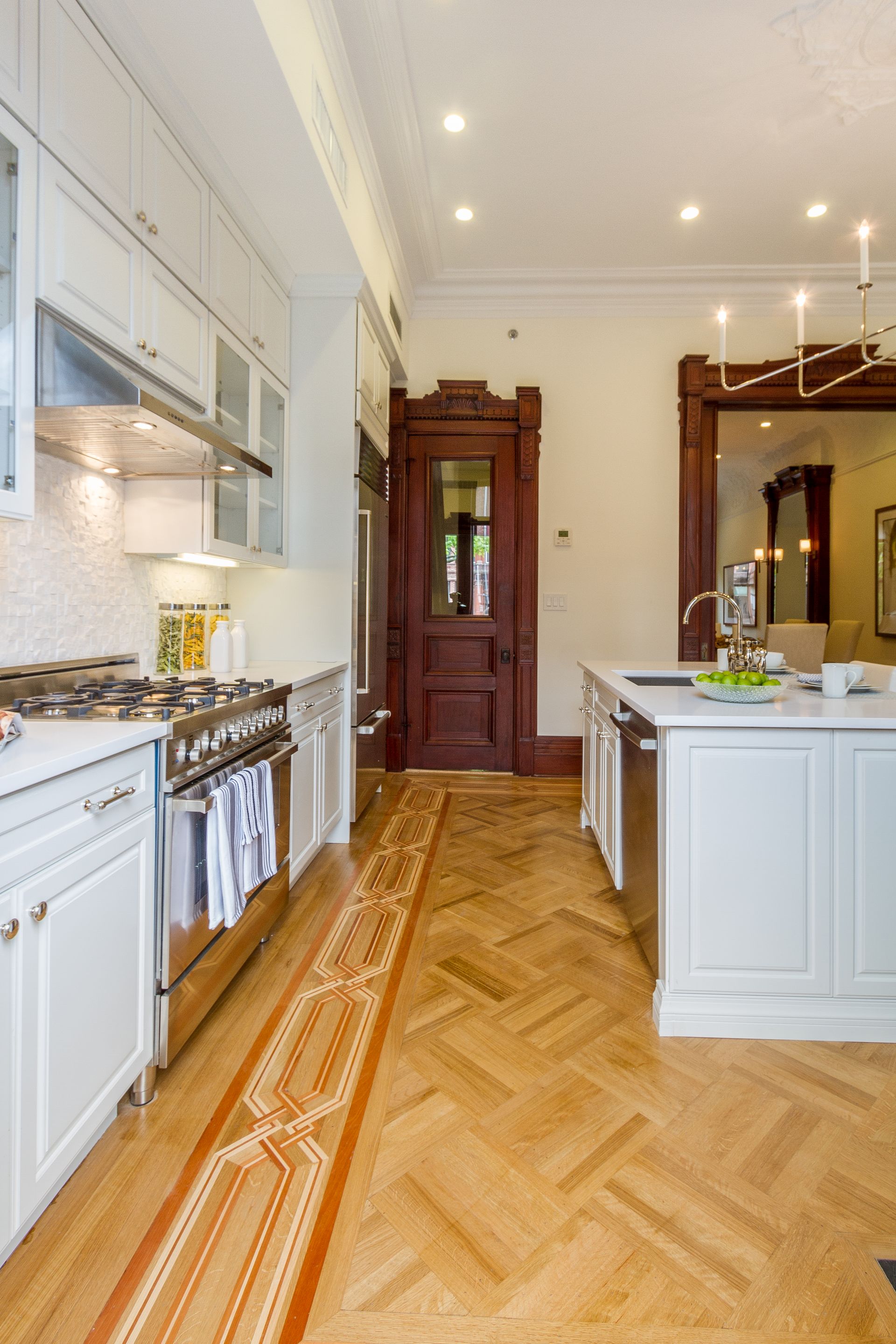 Kitchen with white cabinets, stainless steel appliances, and herringbone wood floor.