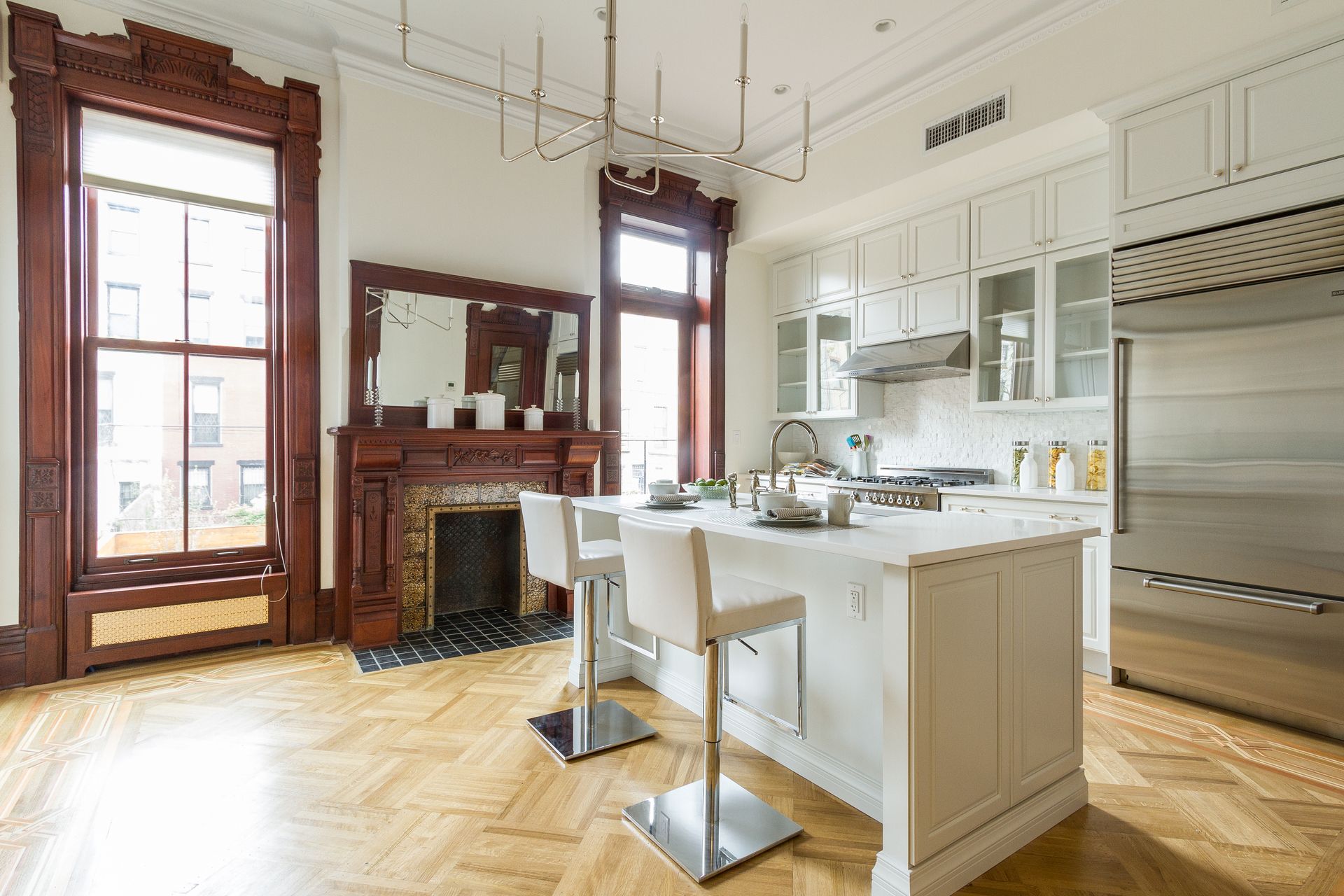 Kitchen with white cabinets, island, and wood floors. Dark wood trim surrounds windows and fireplace.
