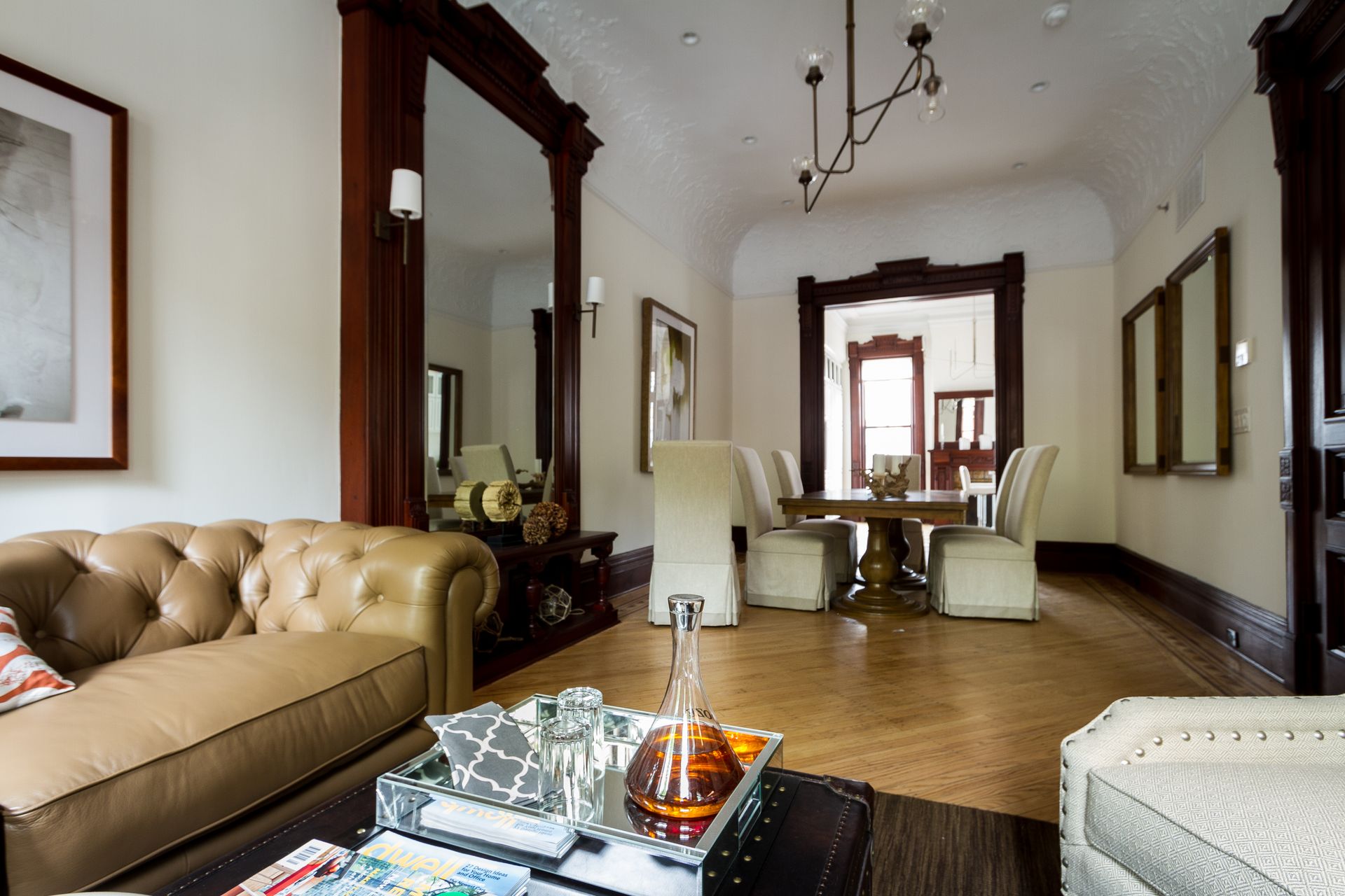 Living room with leather sofa, large mirror, and dining area. Wooden floors, white walls, dark wood trim.