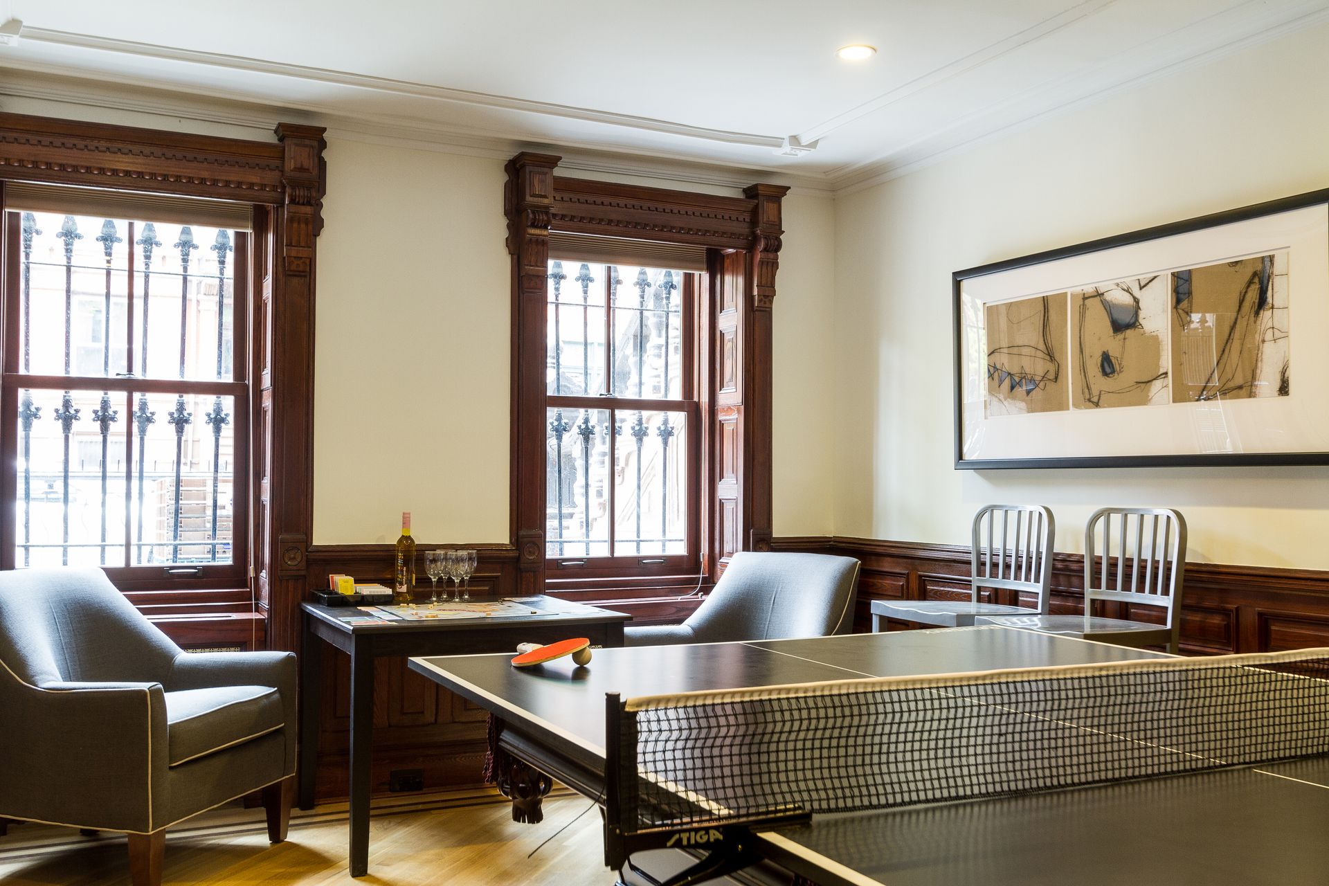 Game room with ping pong table, armchairs, and framed art; dark wood trim and windows.