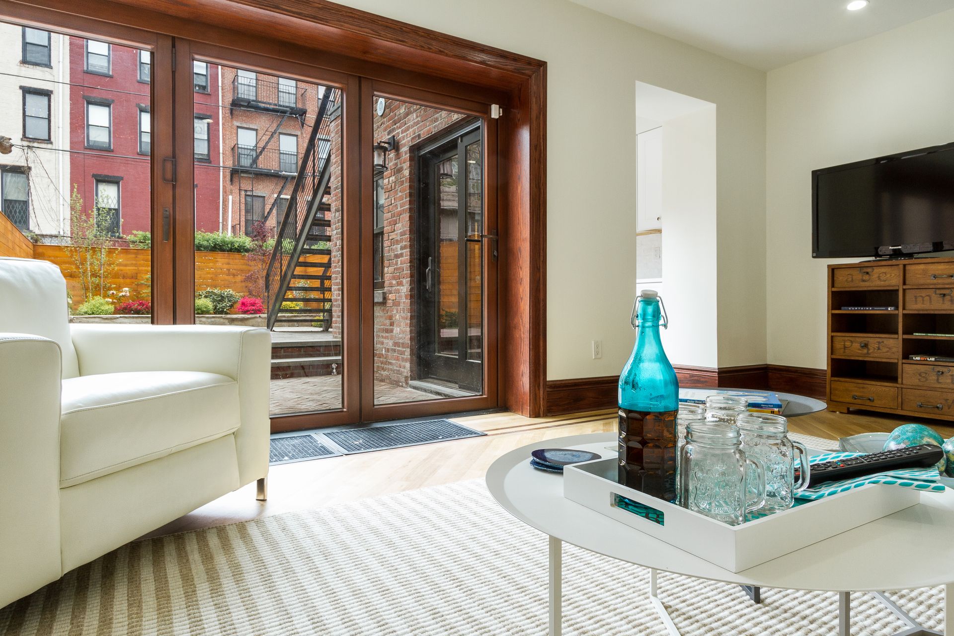 Living room with sliding glass door to a patio; white armchair, round coffee table, TV, wooden floor.