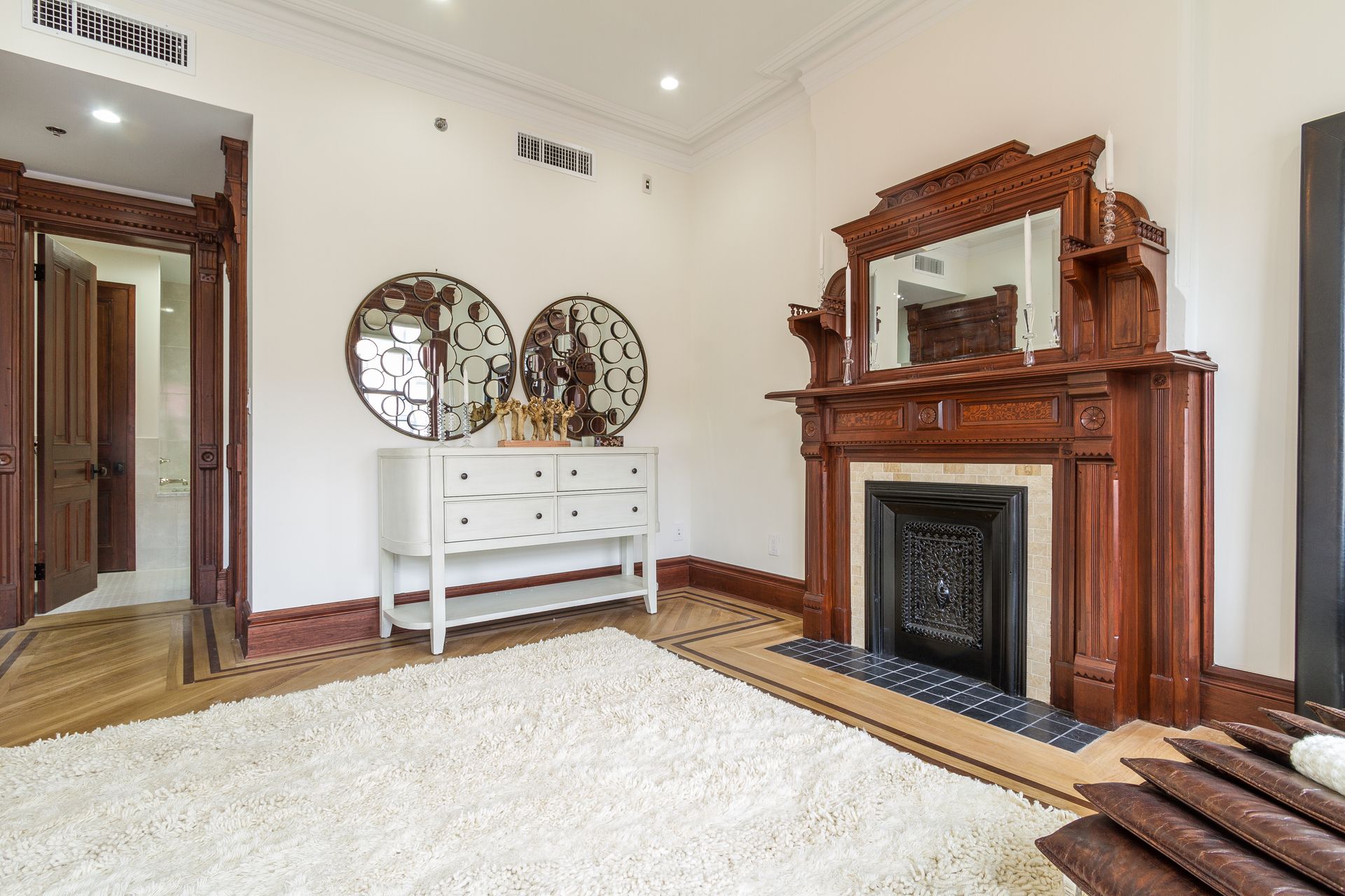 Room with a white dresser, large decorative mirrors, and a dark wood fireplace.