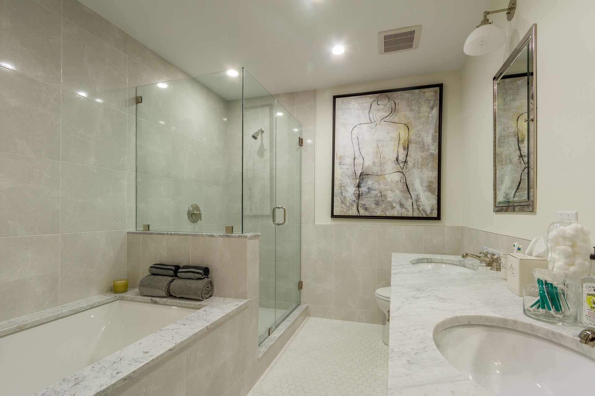 Bathroom with a tub, glass shower, double vanity, and abstract art, all in neutral tones.