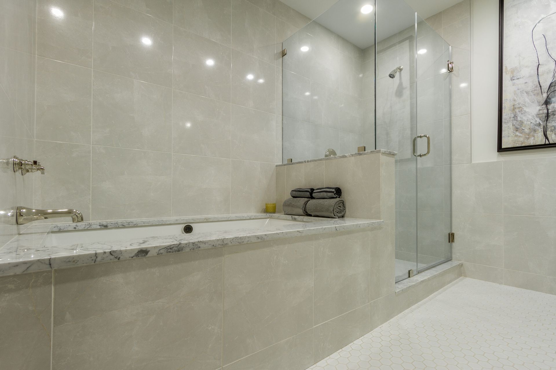 Bathroom with a bathtub and glass shower; neutral-toned tile and countertops.