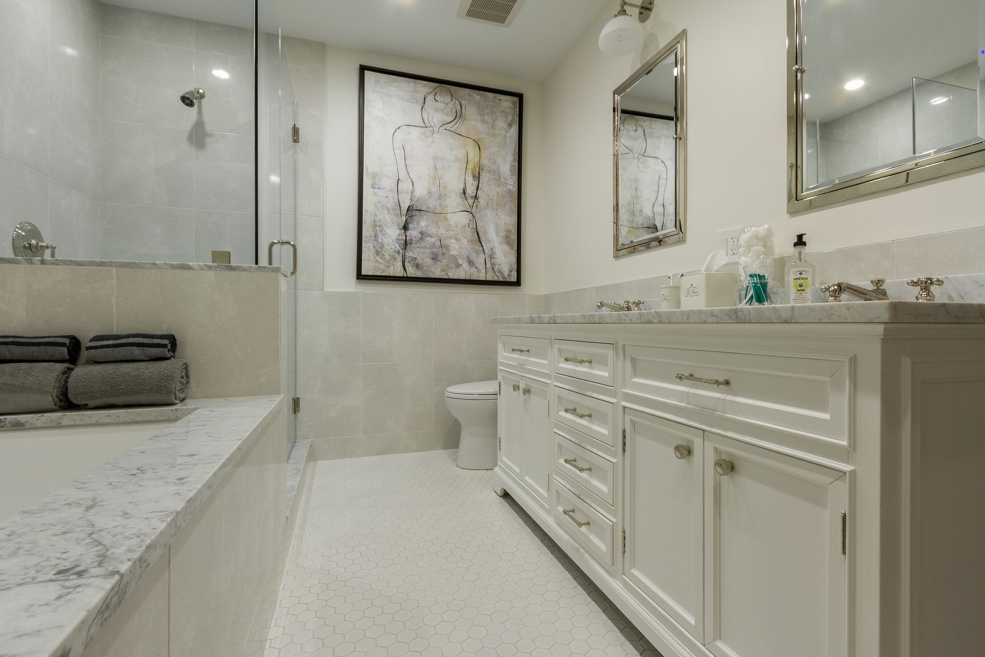 White bathroom with marble accents, double vanity, and a shower with glass enclosure.