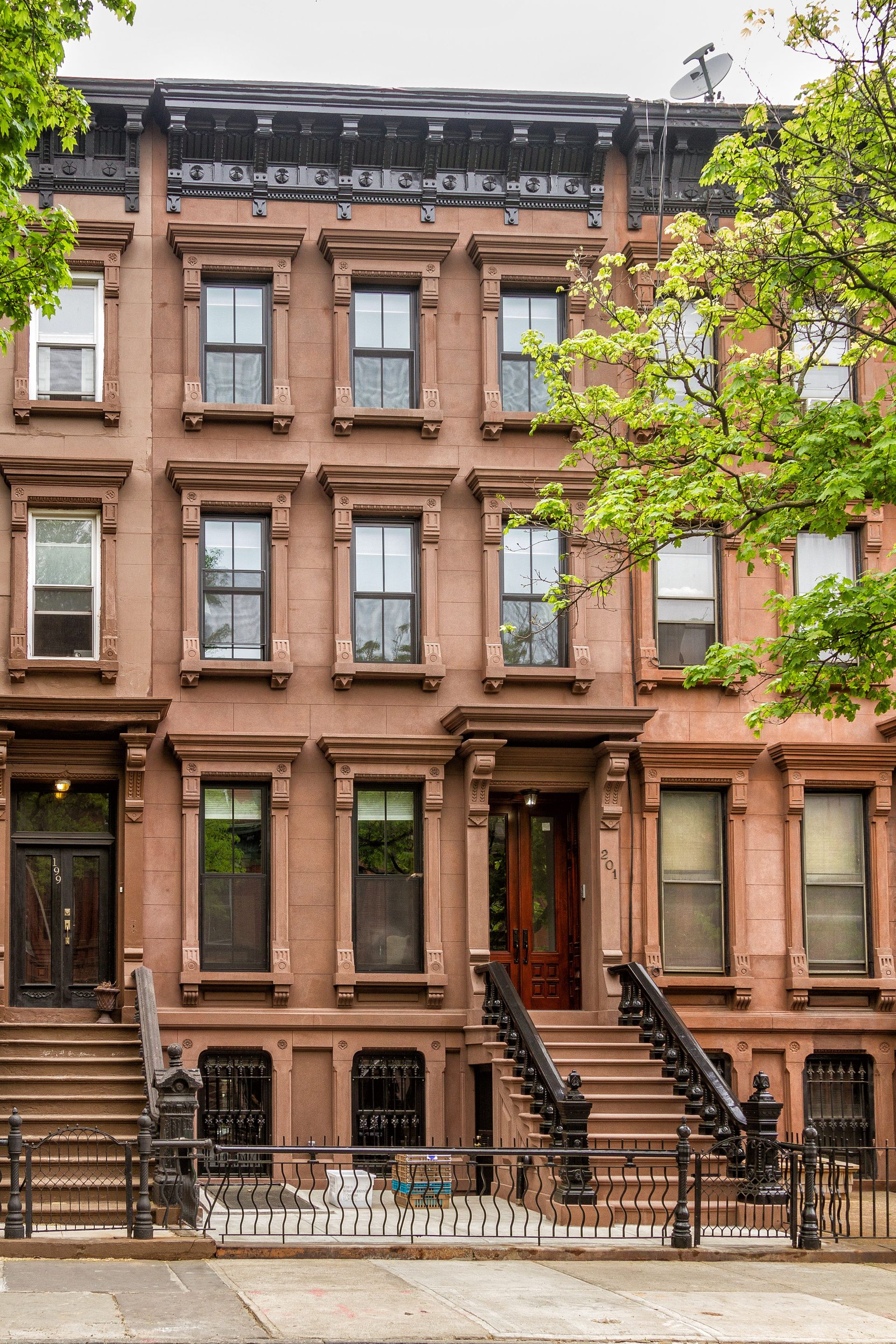 Brownstone buildings with ornate details; street level steps and wrought-iron fence.