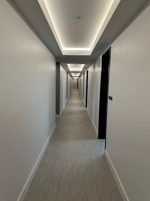 Long, narrow hallway with white walls, recessed ceiling lights, and doors on the right.