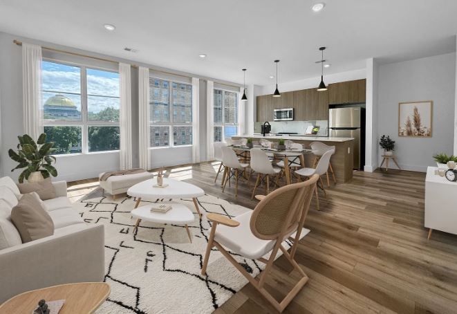 Modern open-plan living space with kitchen, dining area, and living room. Neutral colors, large windows, wood floors.