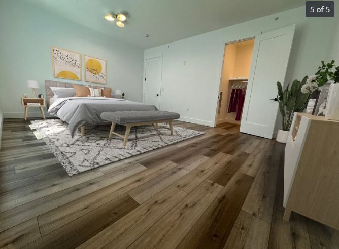 Bedroom with wood floors, bed, rug, closet, and dresser. Soft blue walls and natural light.