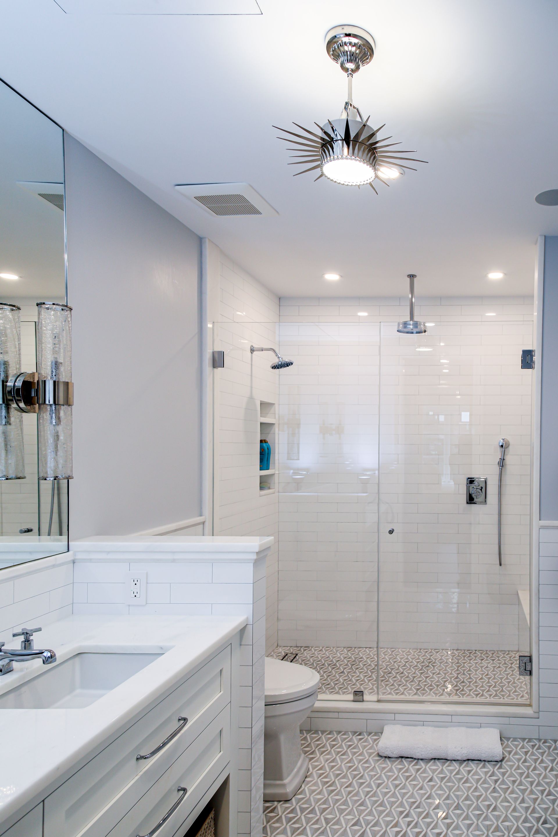 Modern, white bathroom with a glass shower, white vanity, and pebble floor. Chrome fixtures and sunburst ceiling light.