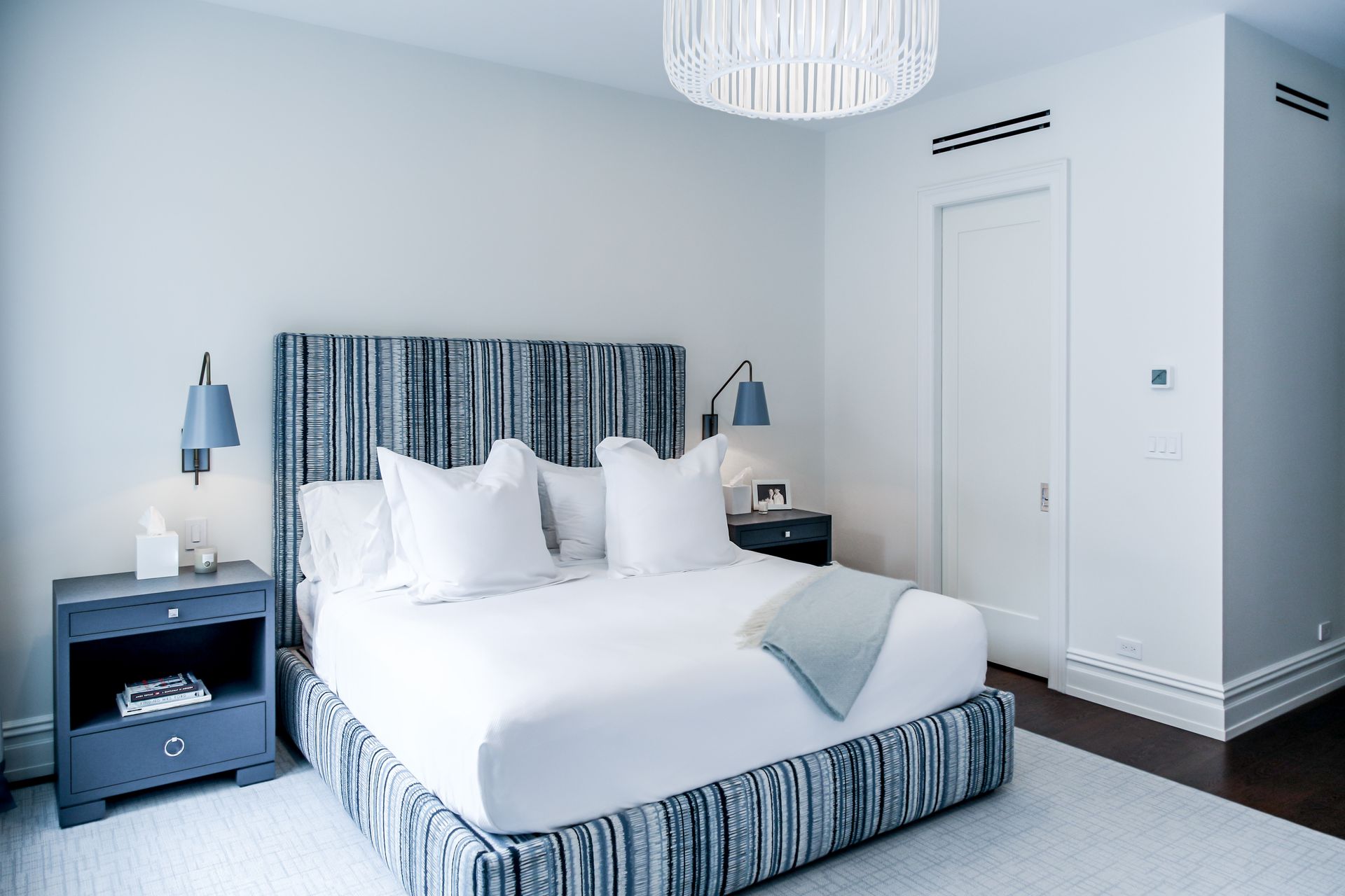 Bedroom with blue-striped upholstered bed, white bedding, and two bedside tables. A chandelier hangs above the bed.