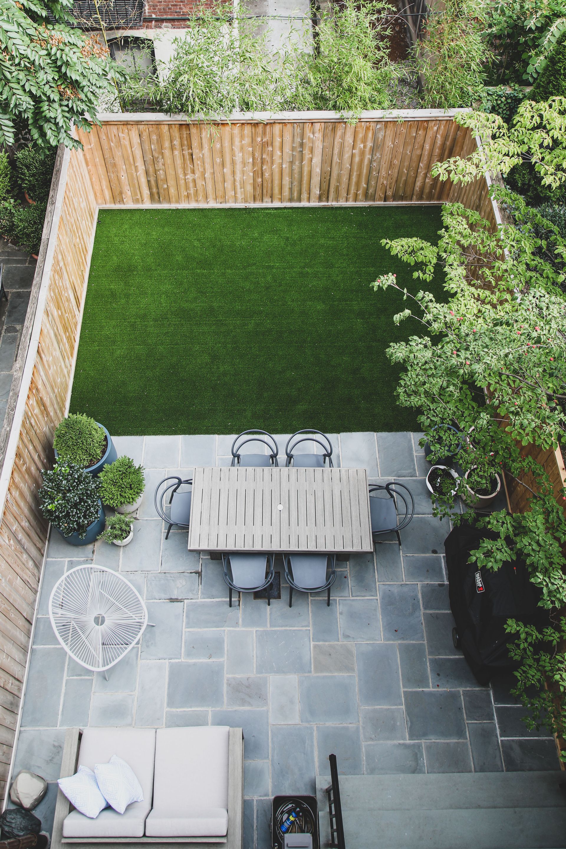 Overhead view of a backyard with a dining table, seating, a grass area, and a wooden fence.