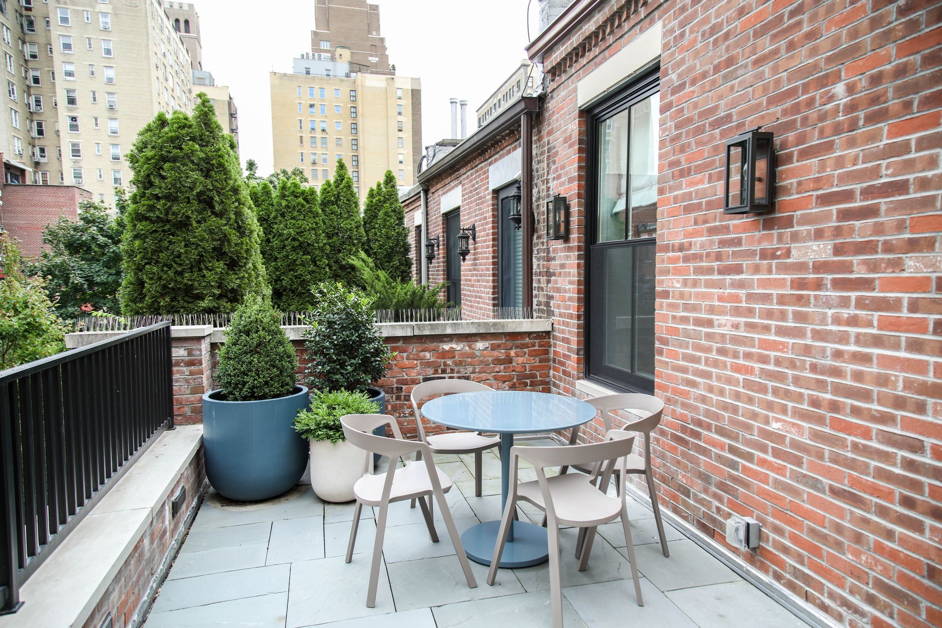 Terrace with blue table and chairs, brick wall, and potted greenery.