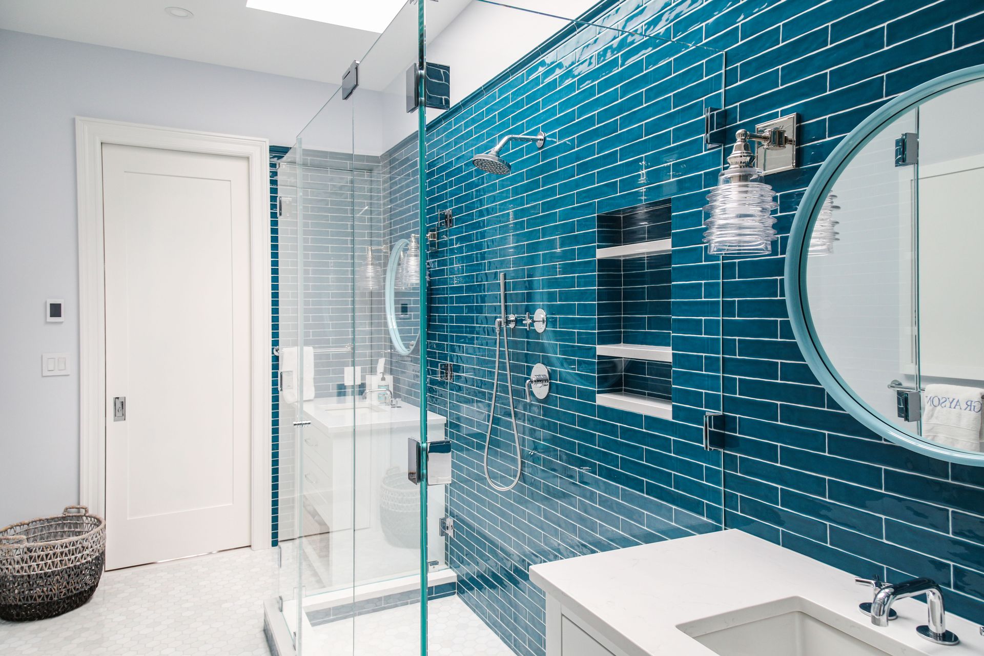 Bathroom with blue tiled wall, glass shower, white vanity, and round mirror.