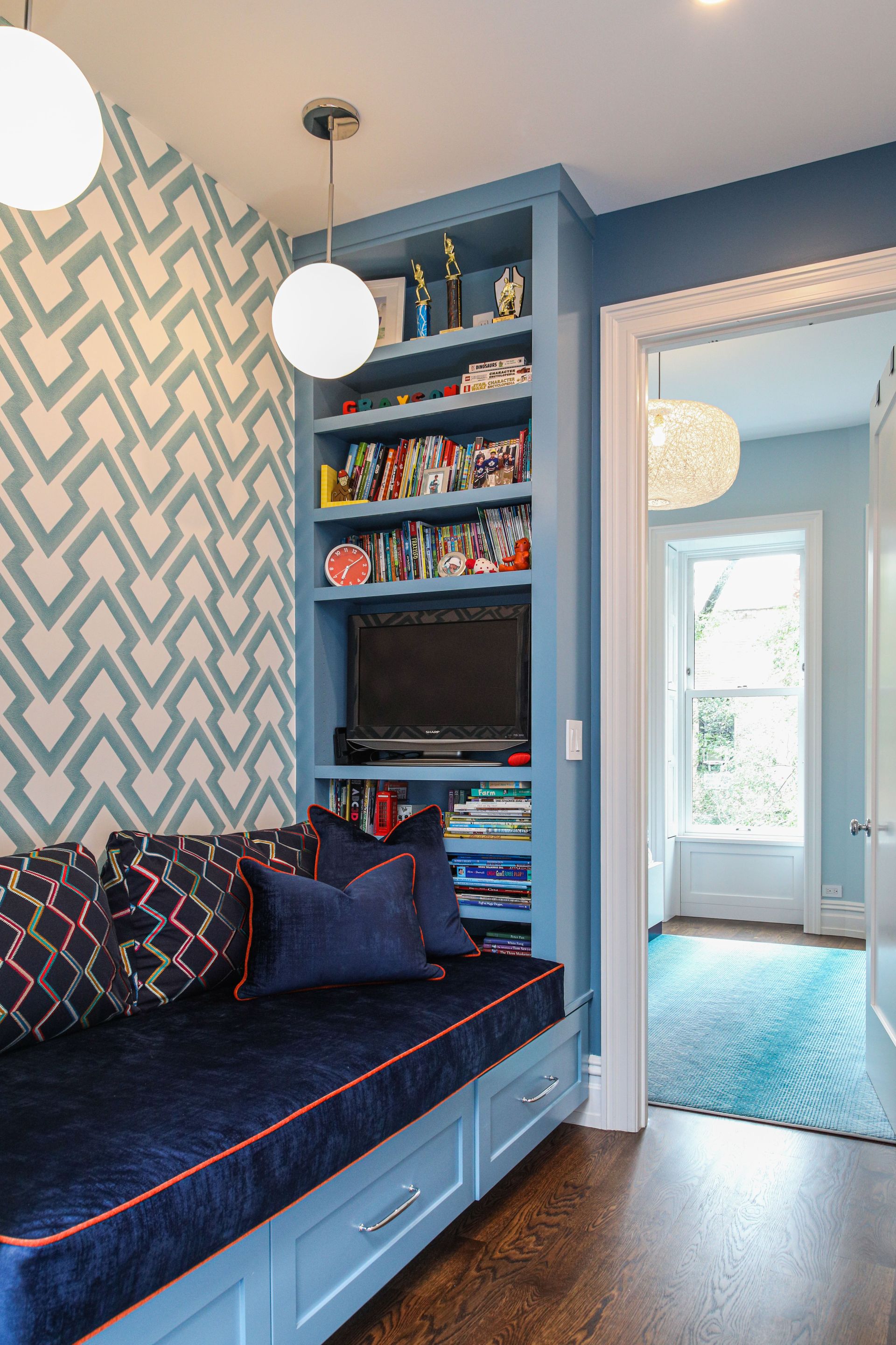 Blue built-in reading nook with patterned wallpaper, shelving, and TV.