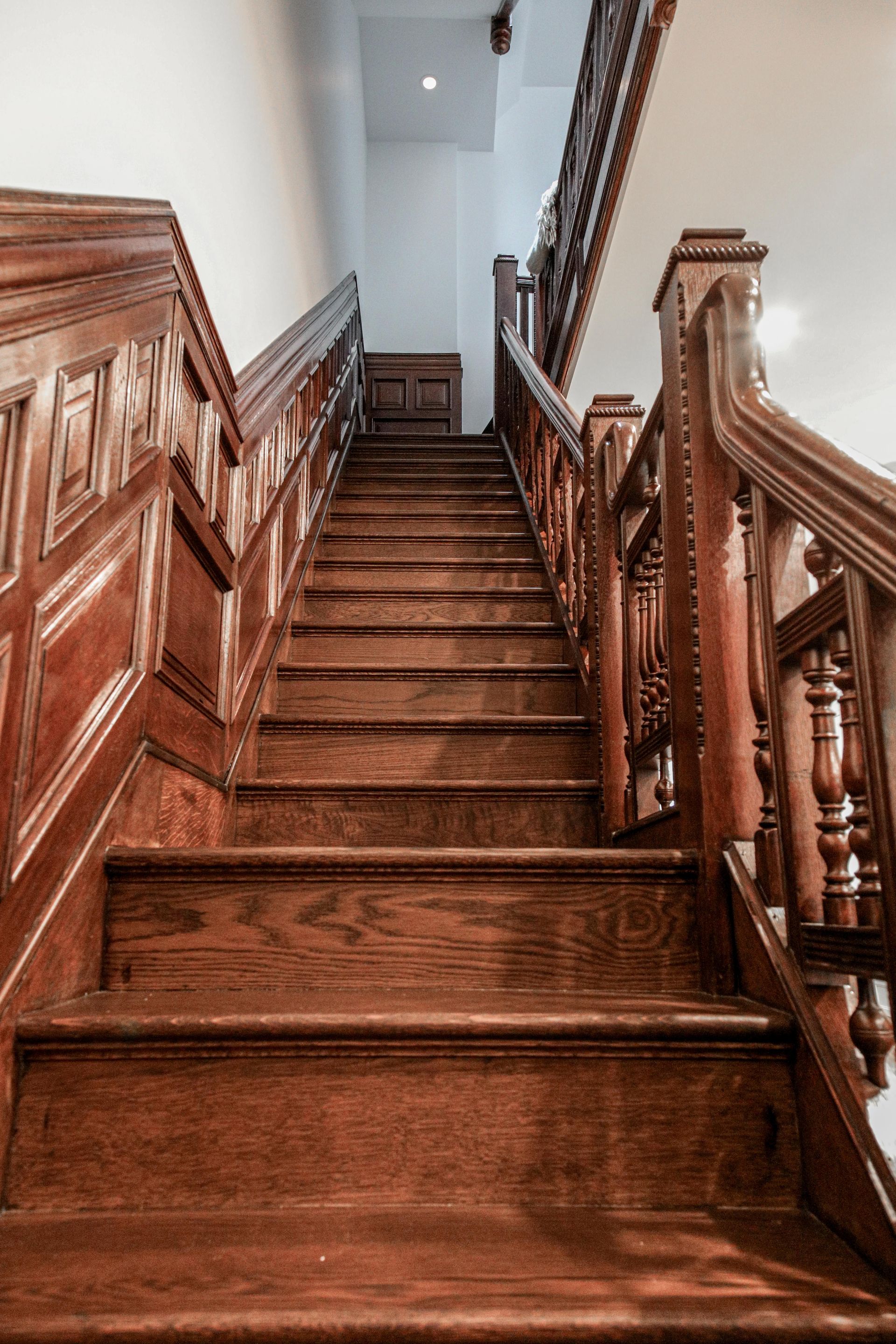 Wooden staircase with intricate railing and paneling, ascending upwards in a building.