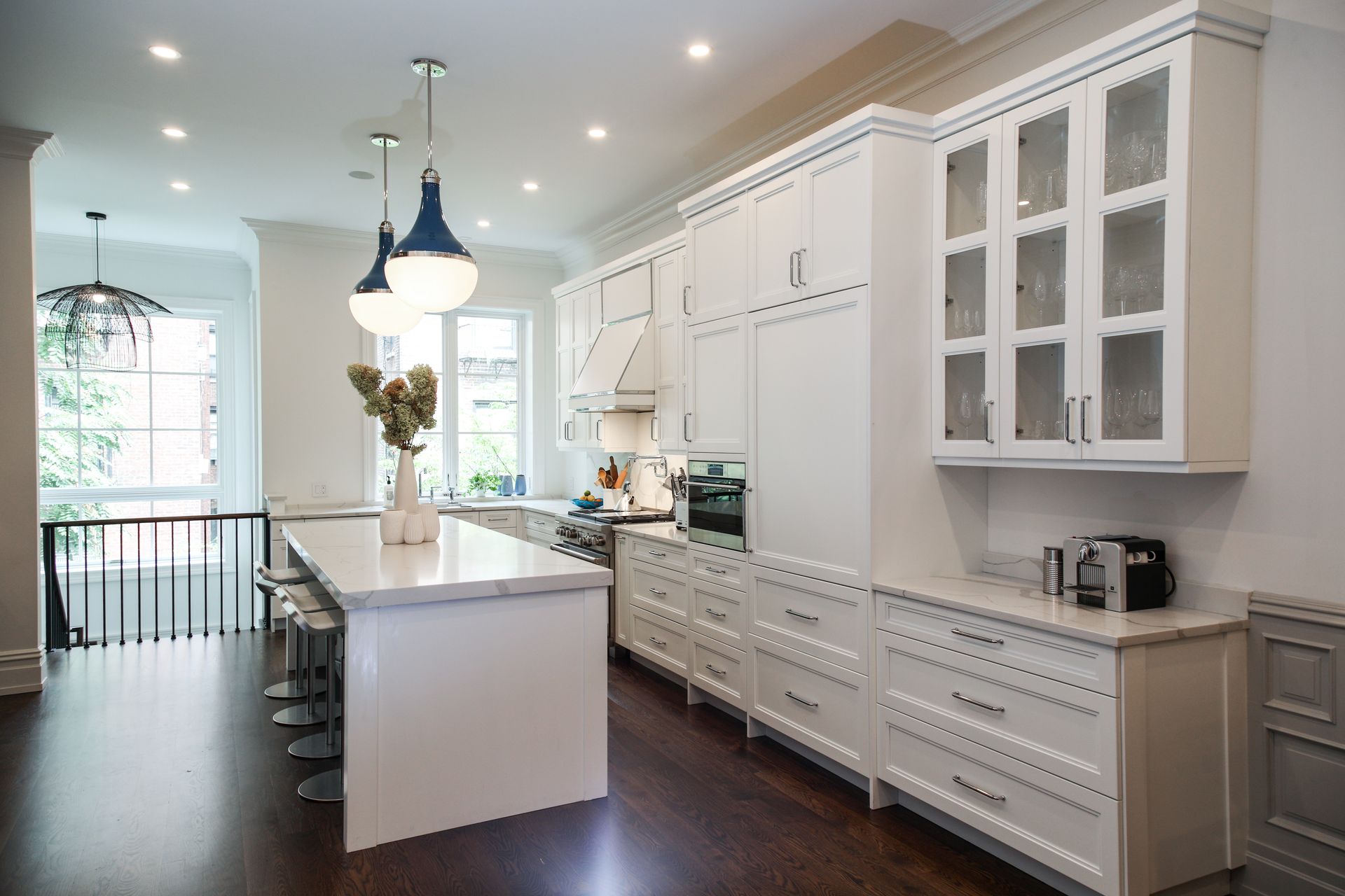White kitchen with island, cabinets, and appliances. Dark wood floor, three blue pendant lights.