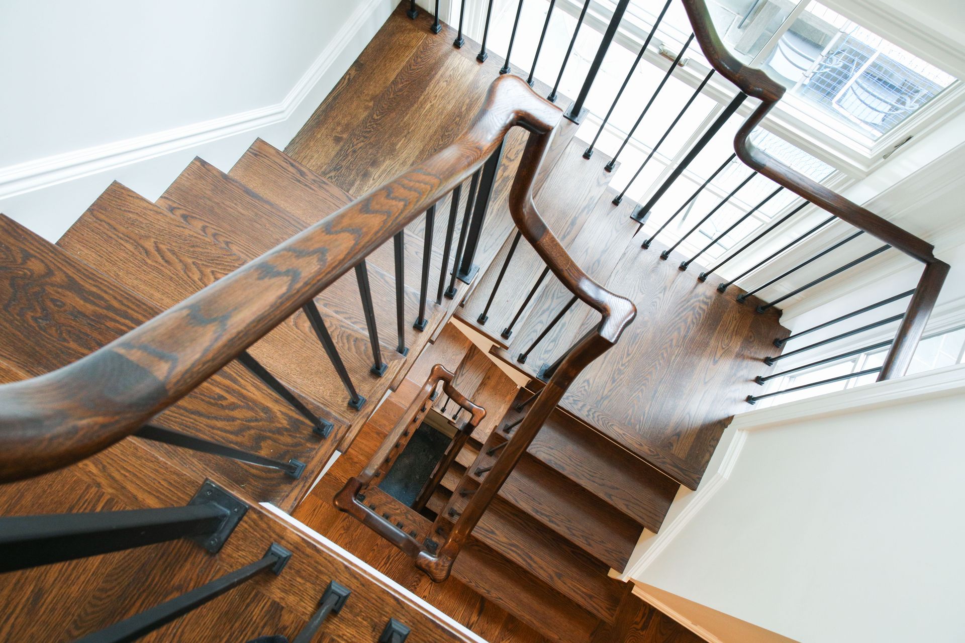 Wooden staircase with dark railing and balusters, viewed from above.
