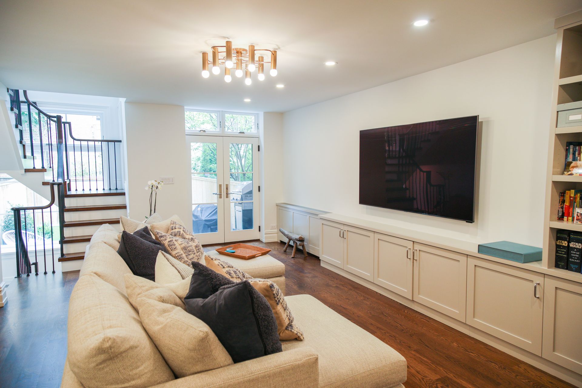 Living room with TV mounted above cabinets, cream sofa, and stairs.