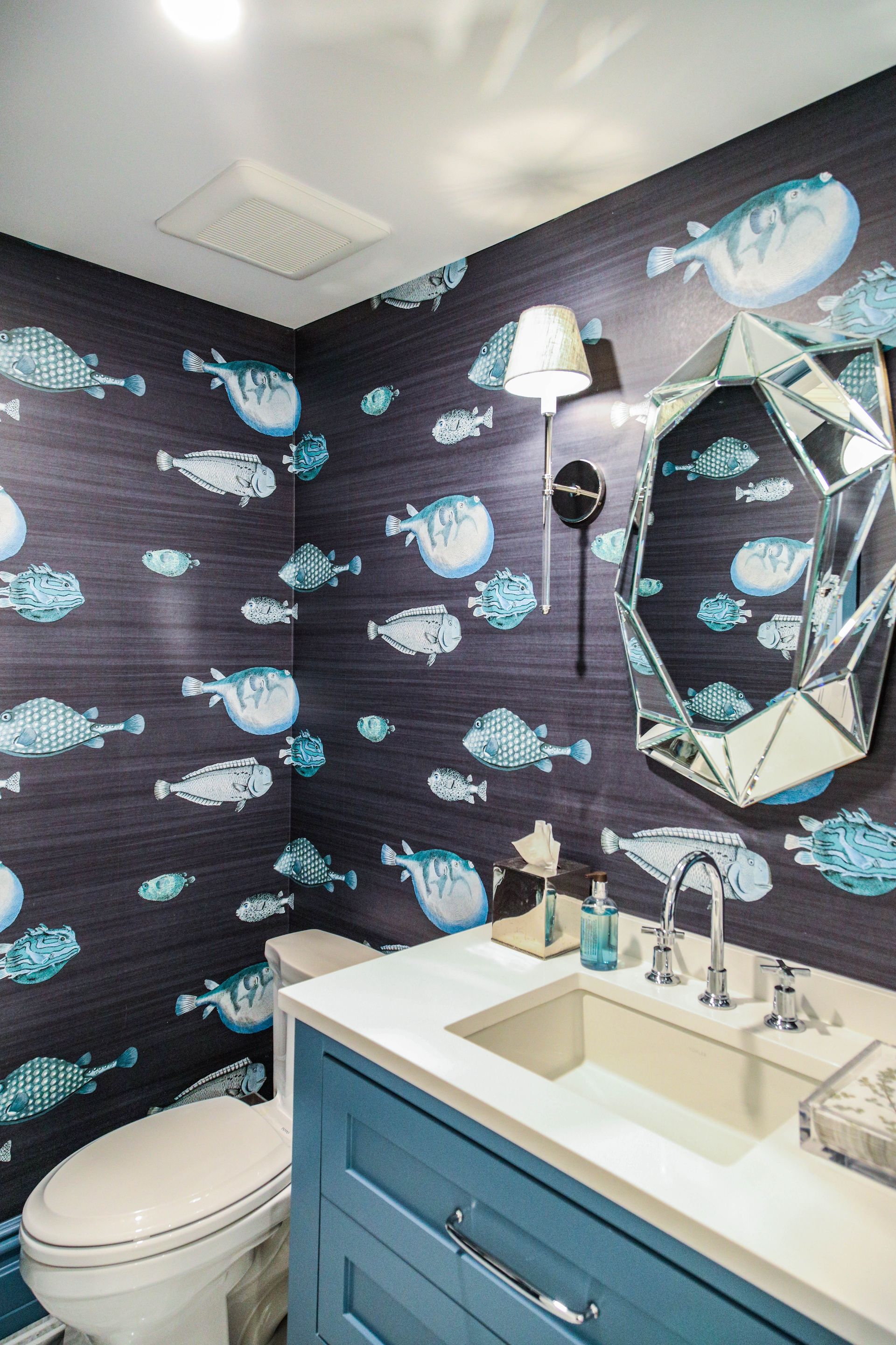 Blue and white fish wallpaper in a bathroom with a blue vanity and an ornate mirror.
