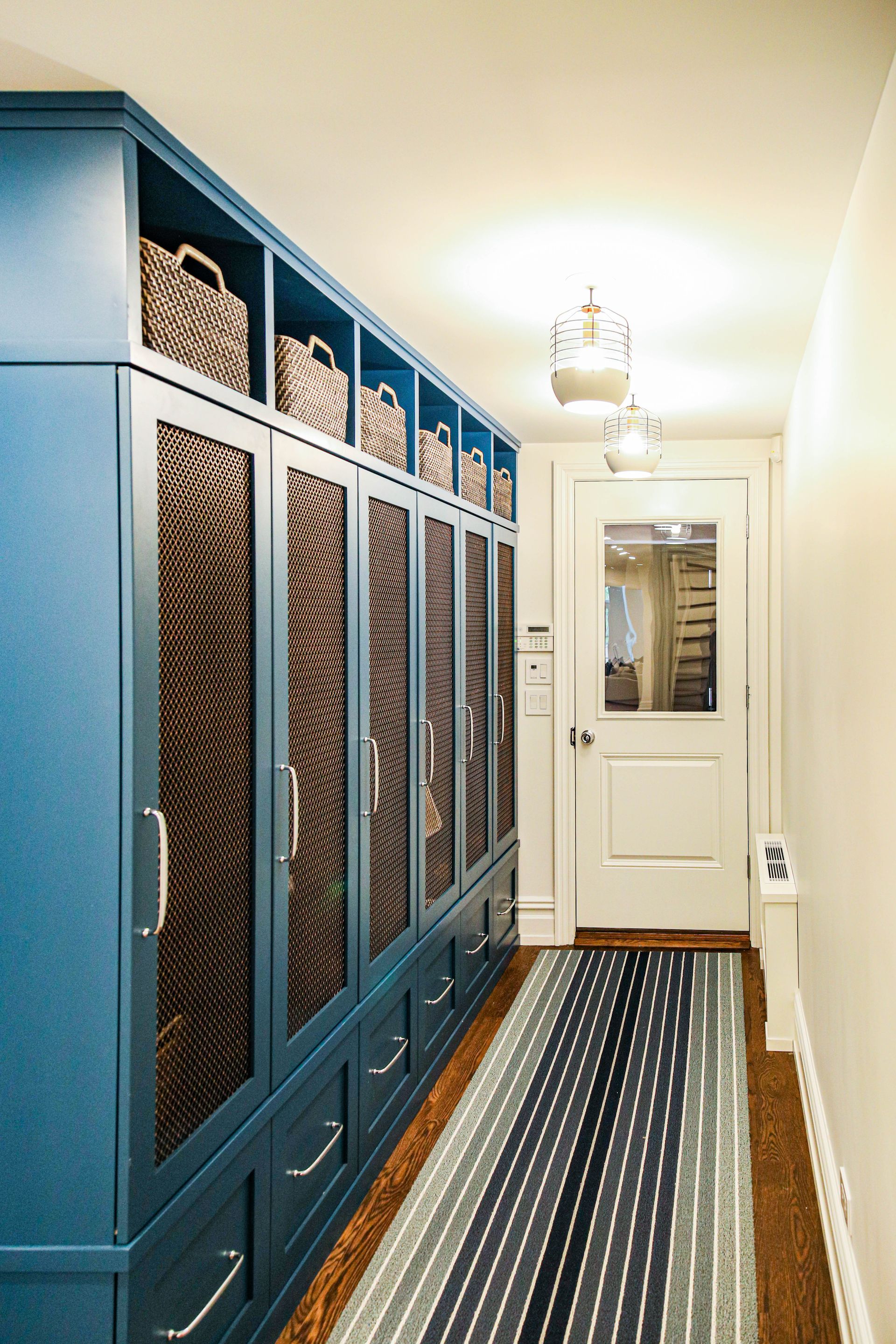 Blue cabinets with woven doors and baskets, a hallway with a striped rug and a white door.