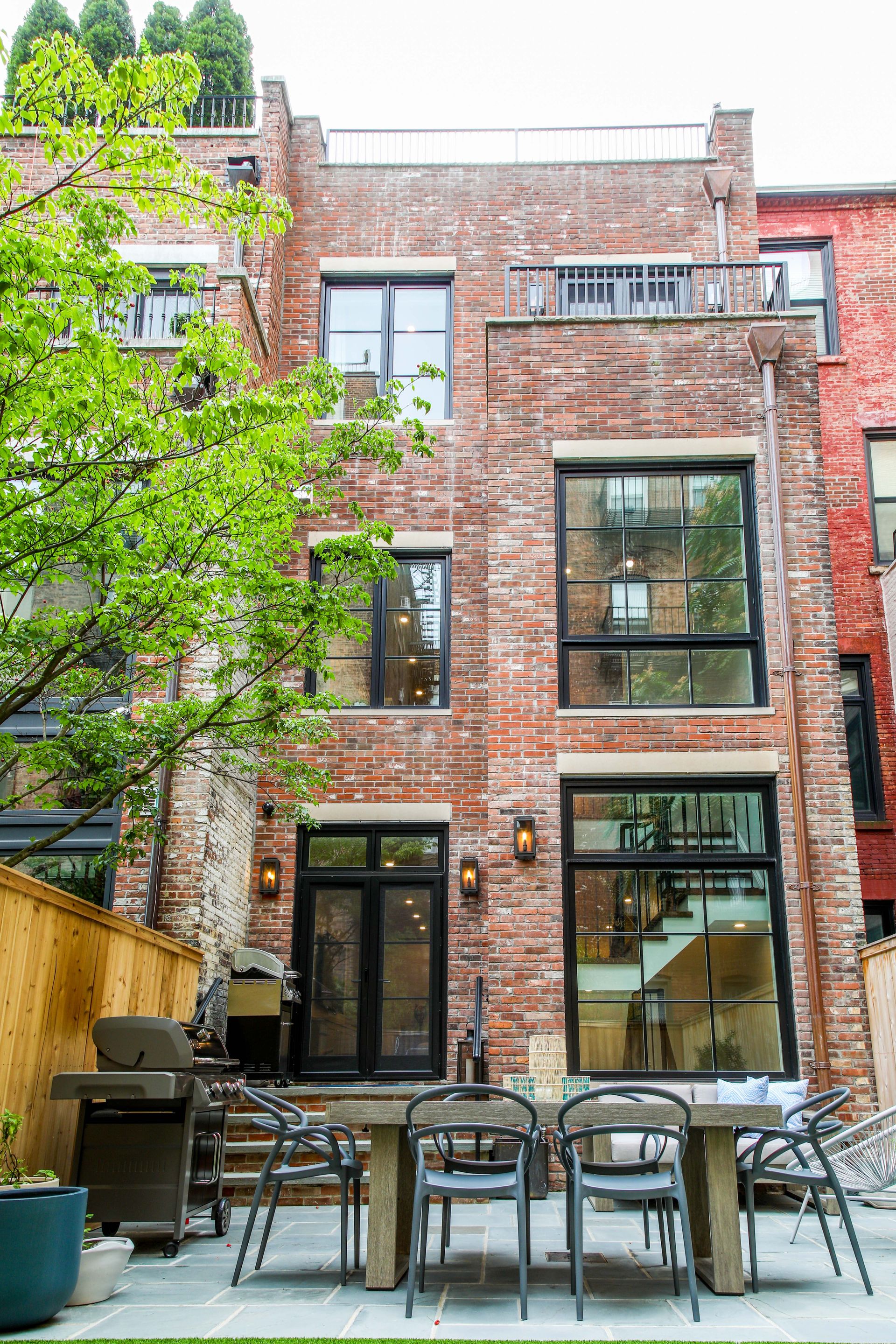 Brick townhouse exterior with patio furniture, large windows, and a small balcony.