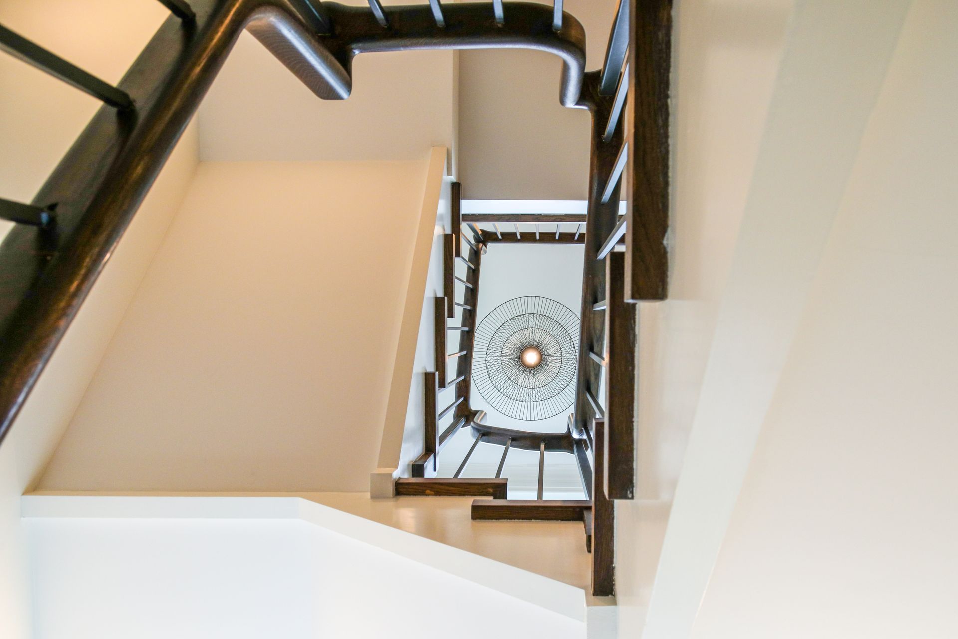 Looking up a wooden spiral staircase with white walls, natural light.