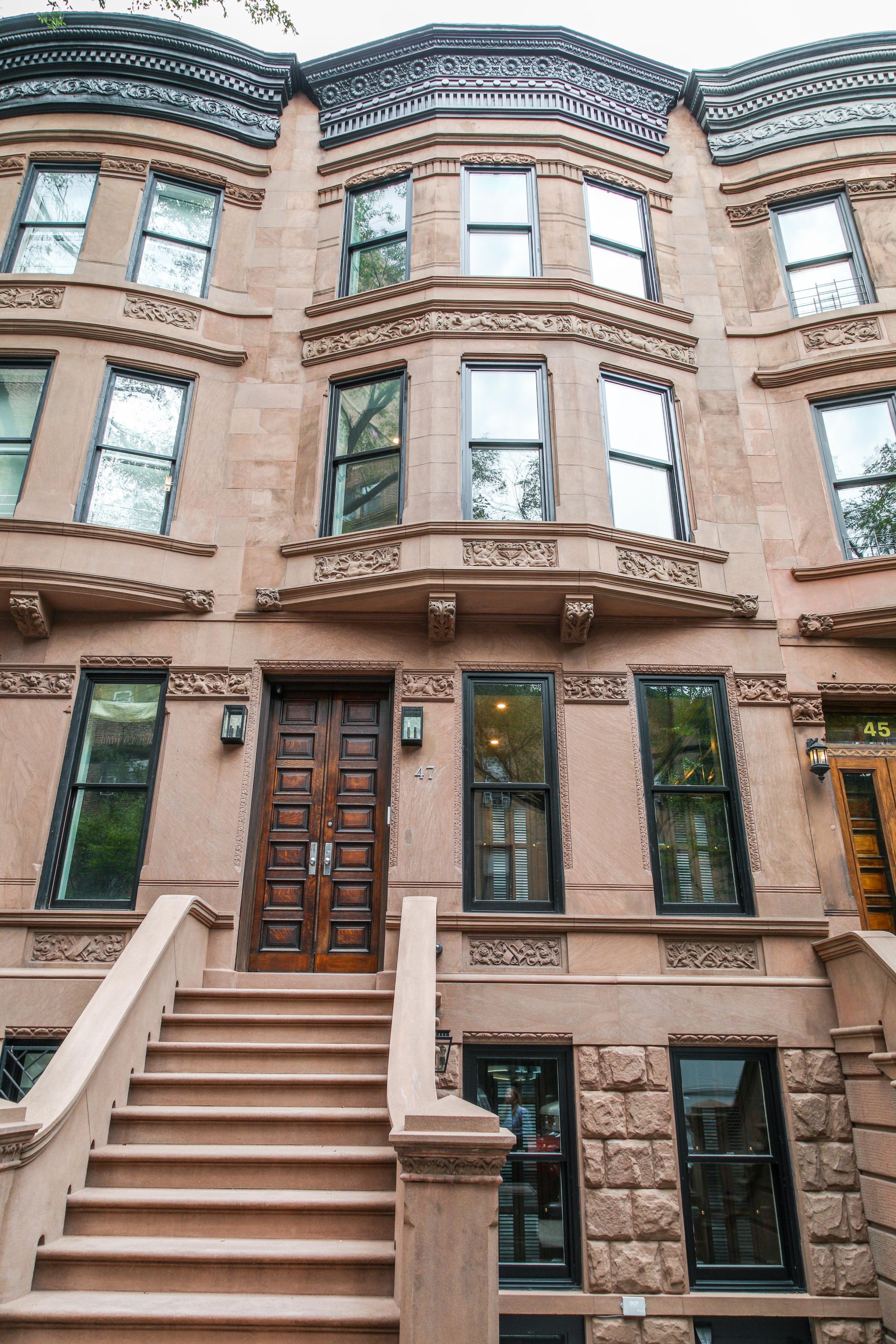 Brownstone building with steps leading to a wooden front door, windows, and decorative facade.