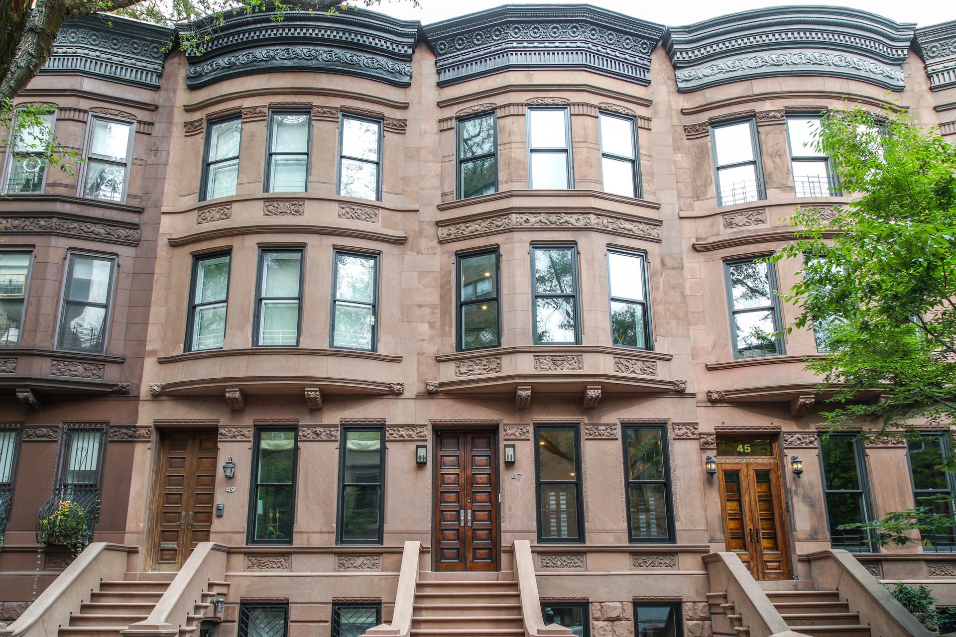Row of brownstone buildings with bay windows, steps, and ornate details.