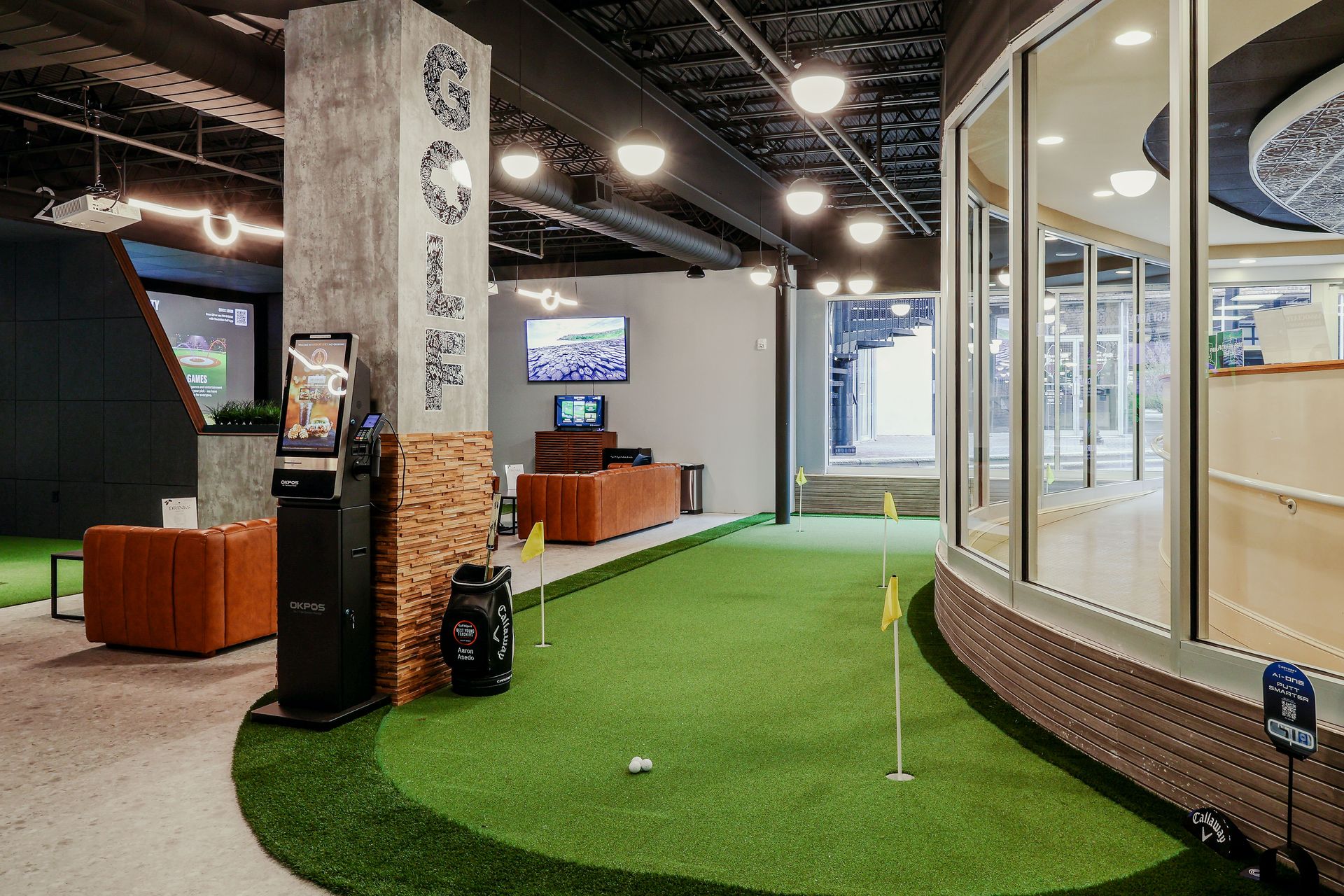 Indoor golf course with putting green, lounge, and view of cityscape.