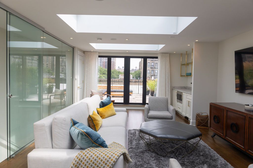 Modern living room with white sofa, blue and yellow pillows, skylights, and glass door to balcony.