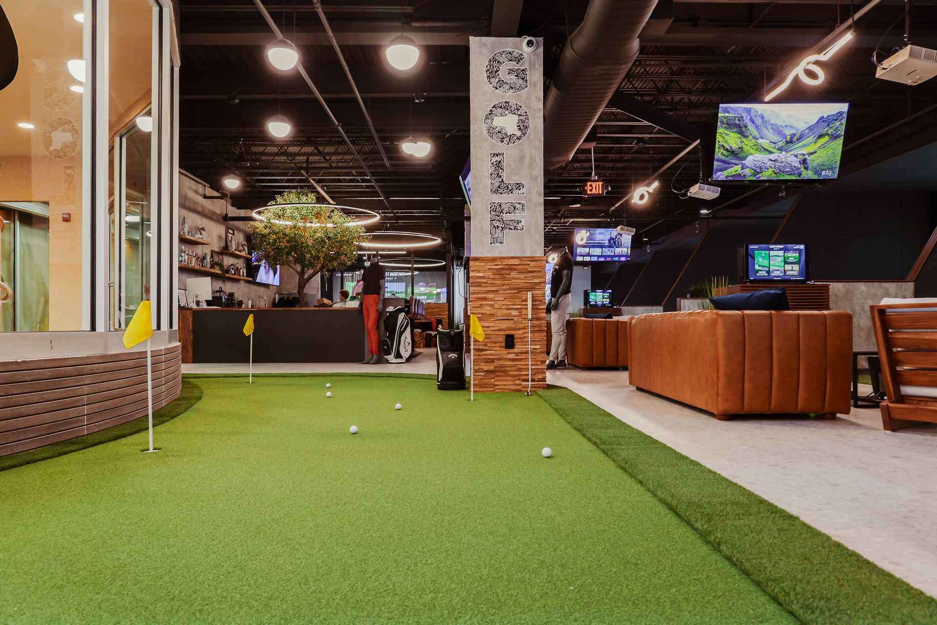 Indoor putting green with golf balls, furniture, TVs, and a bar area.
