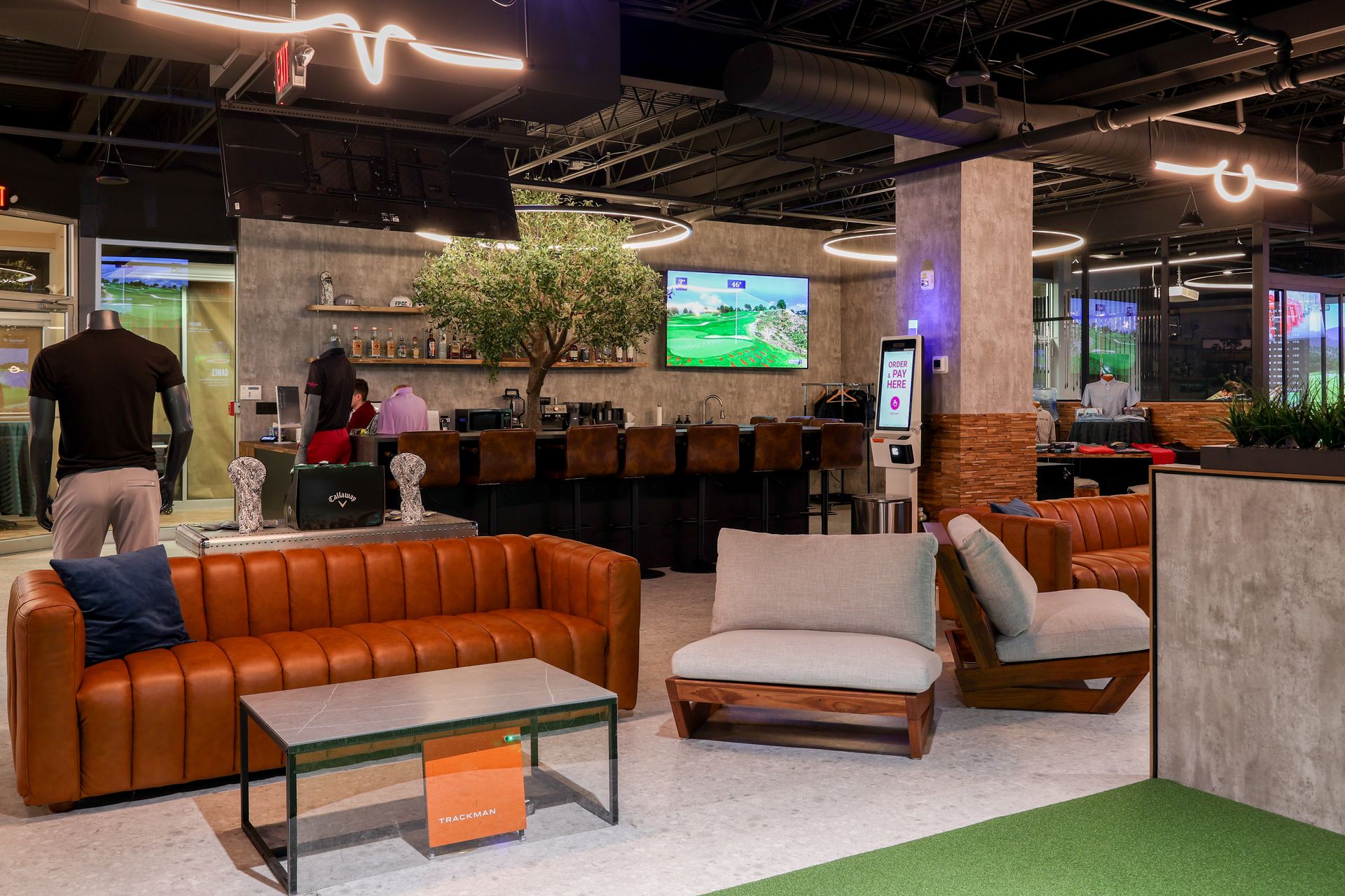 Interior of a golf simulator lounge with leather seating, bar, and TVs displaying golf games.