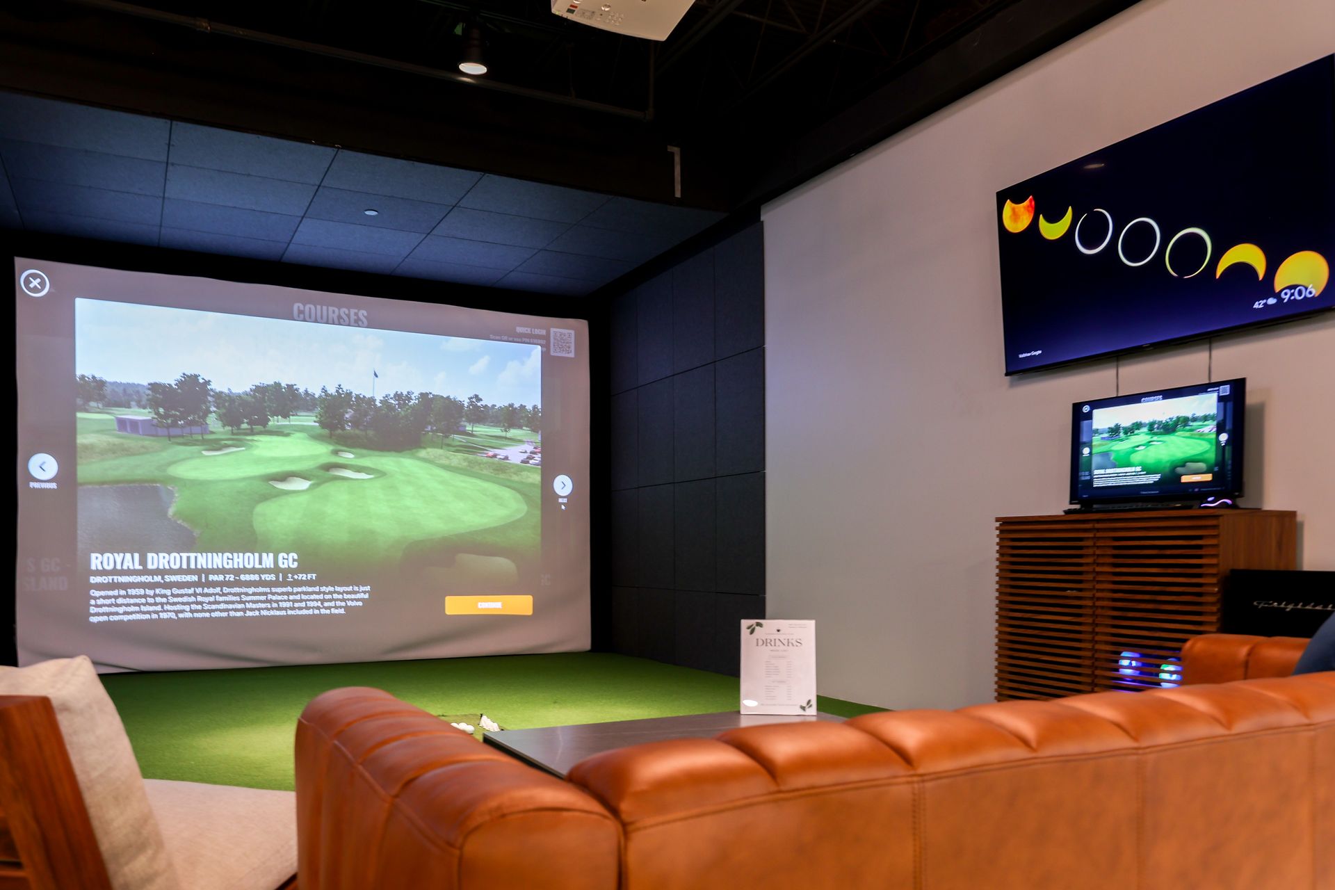 Indoor golf simulator with a screen showing a golf course and a couch for viewing.