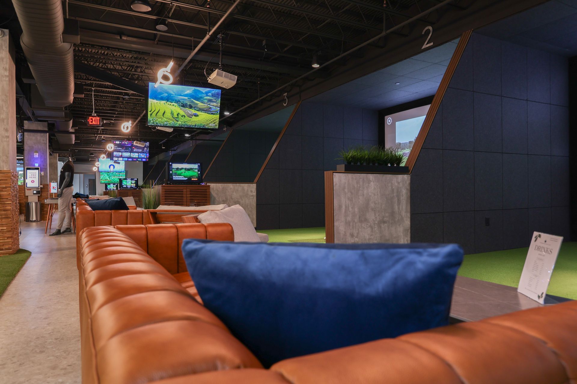 Indoor golf simulator lounge with leather seating, screens, and artificial turf.