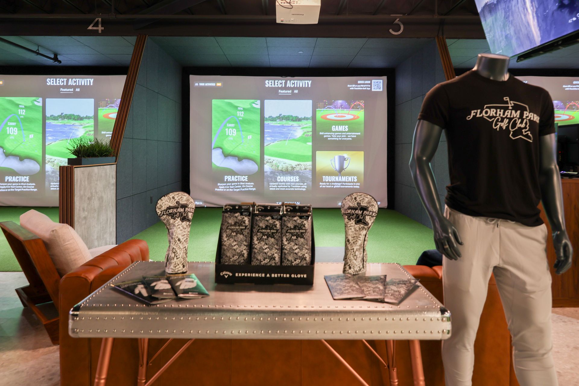Golf simulator room with screens, a table with trophies, and a mannequin wearing a t-shirt and pants.