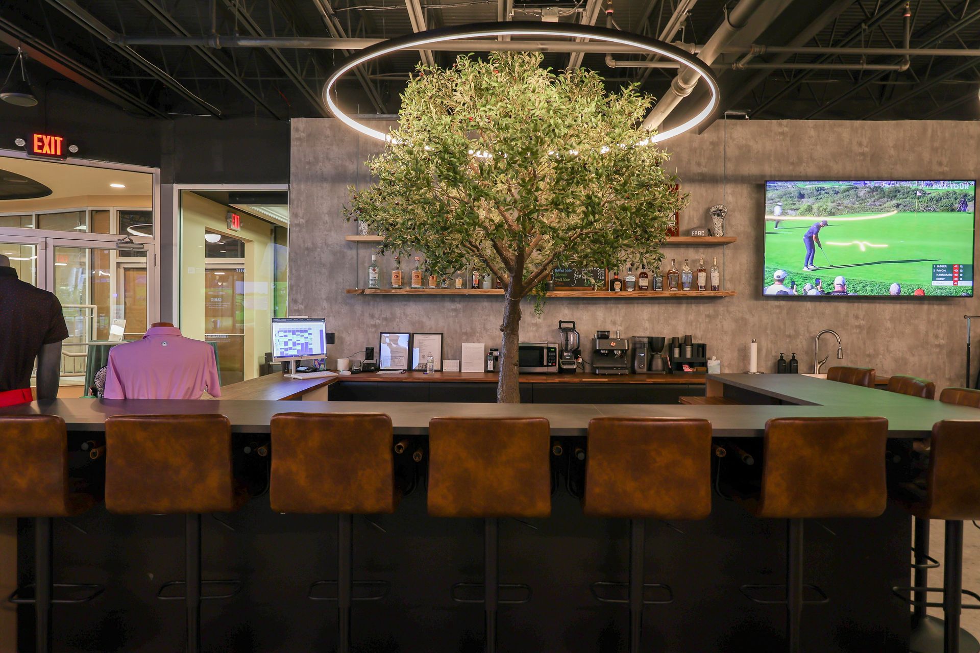 Bar with brown stools, olive tree, bottles, TV showing golf, and a circular light fixture.