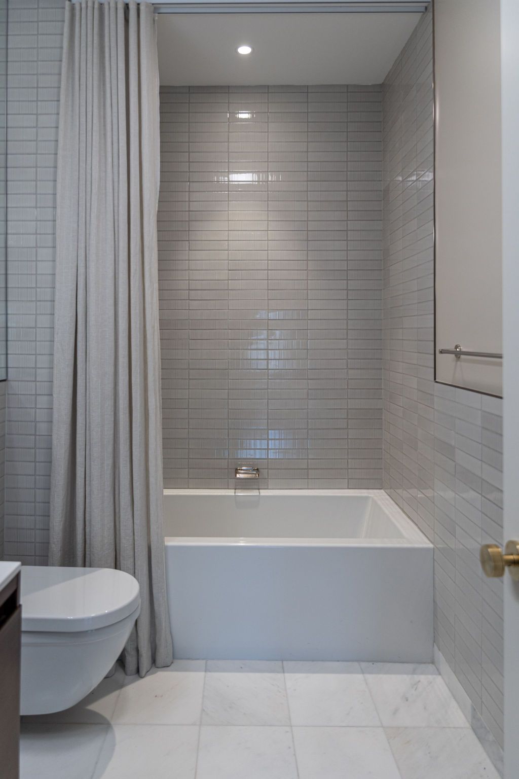 Small bathroom with white bathtub, gray tiled walls, toilet, and shower curtain.