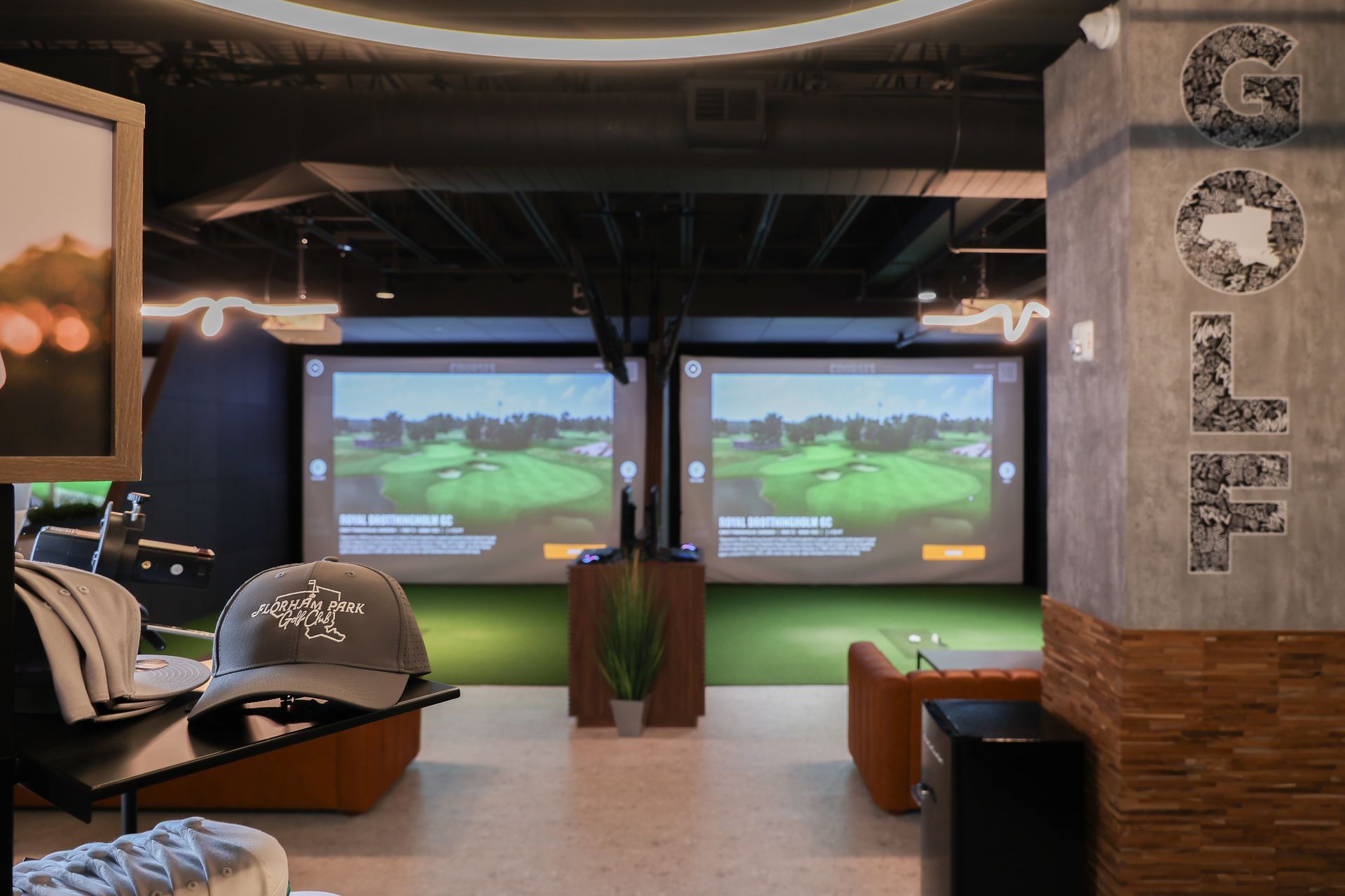 Indoor golf simulator room with screens displaying a golf course, seating areas, and
